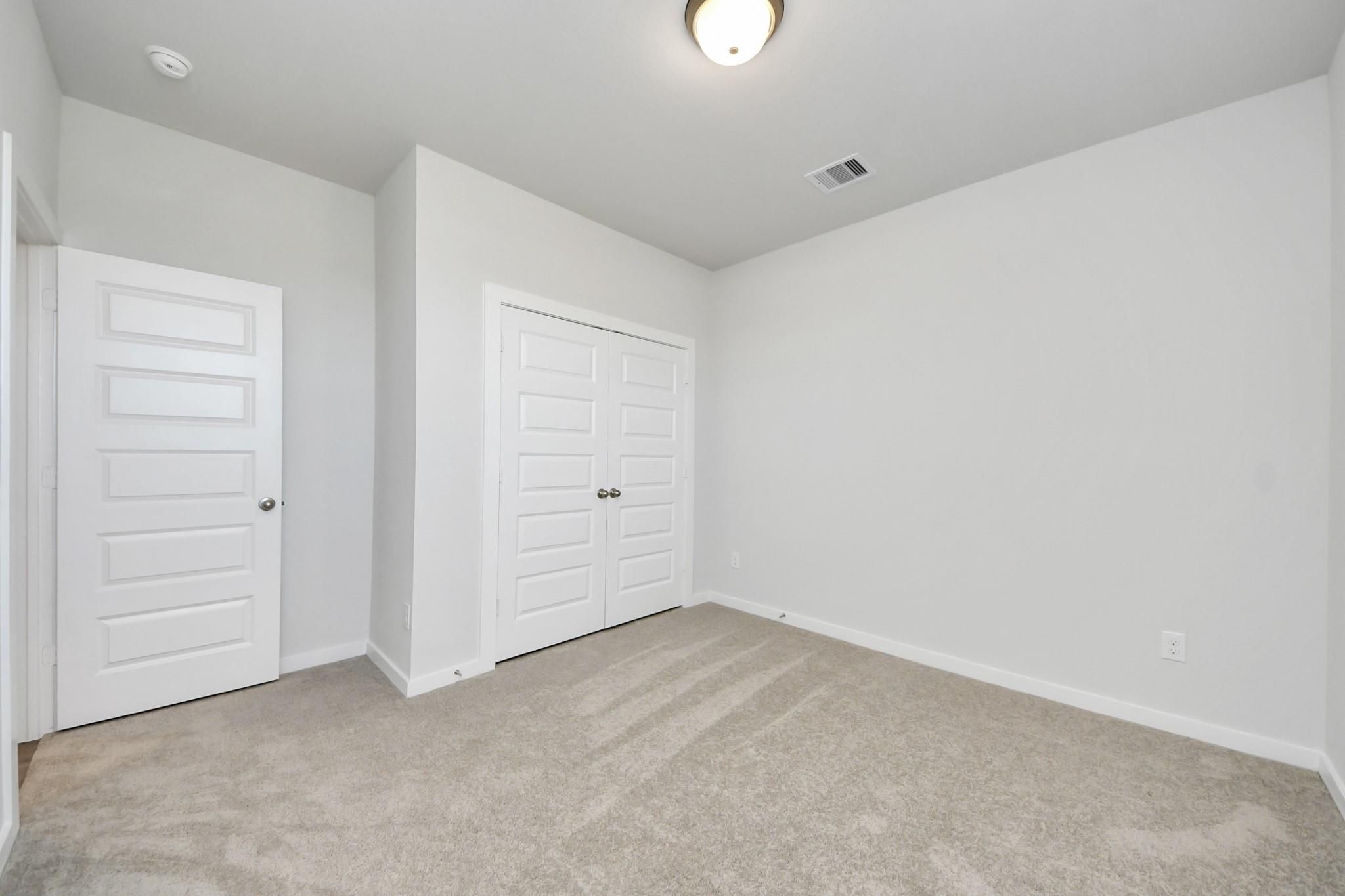 Bright carpeted bedroom with white double closet doors in Davidson Homes' Costa A plan at Emberly, Beasley, TX