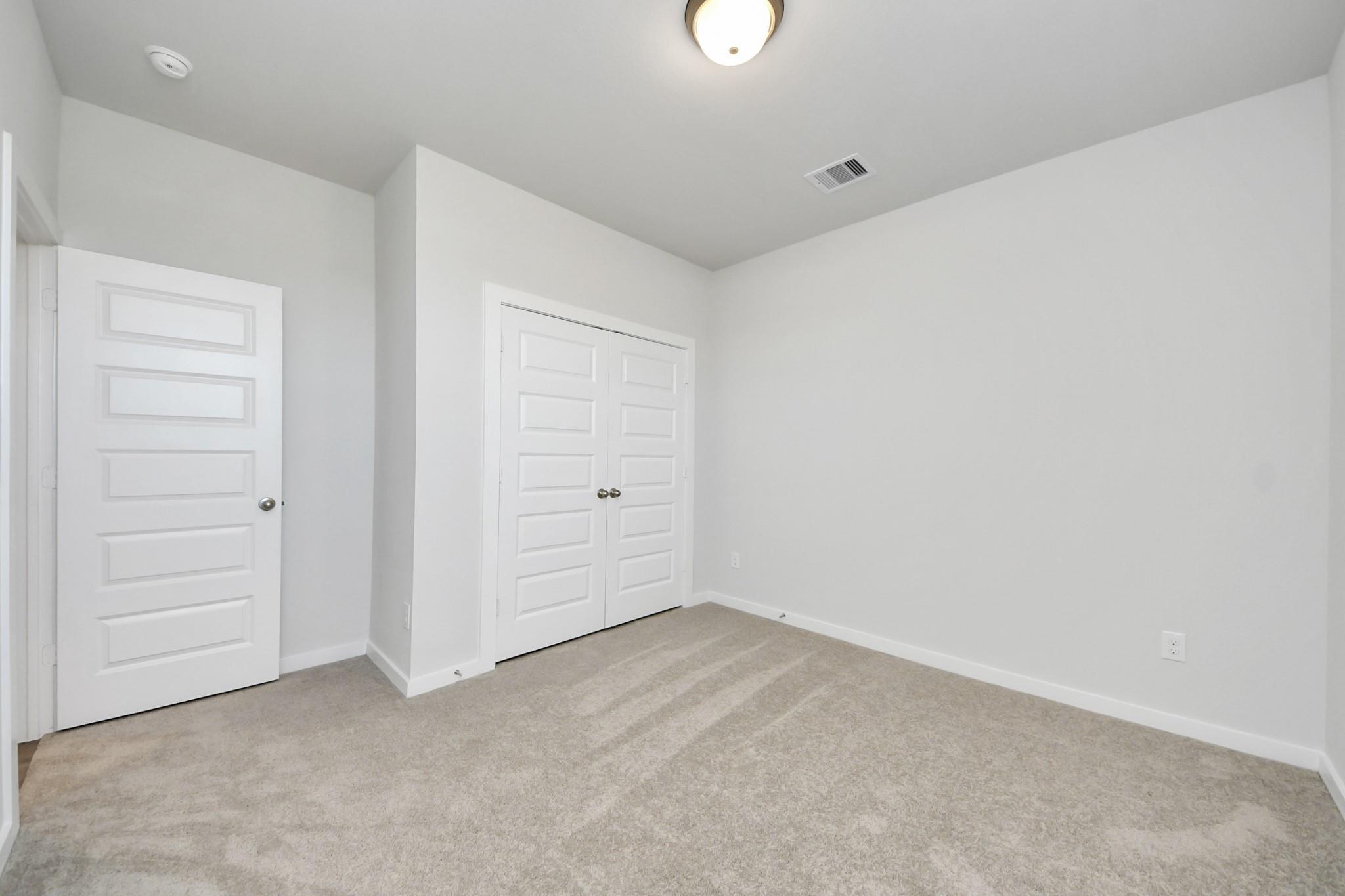 Bright carpeted bedroom with white double closet doors in Davidson Homes' Costa A plan at Emberly, Beasley, TX