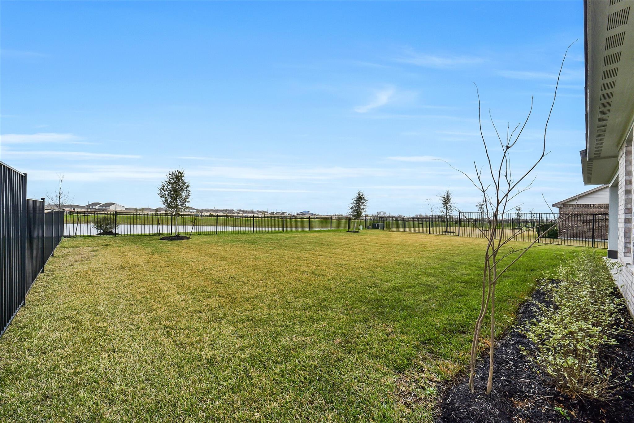 Expansive green backyard with black fence, shrubs, and pond view in 4-bedroom Davidson Homes The Philip B, Sierra Vista, Rosharon, Texas