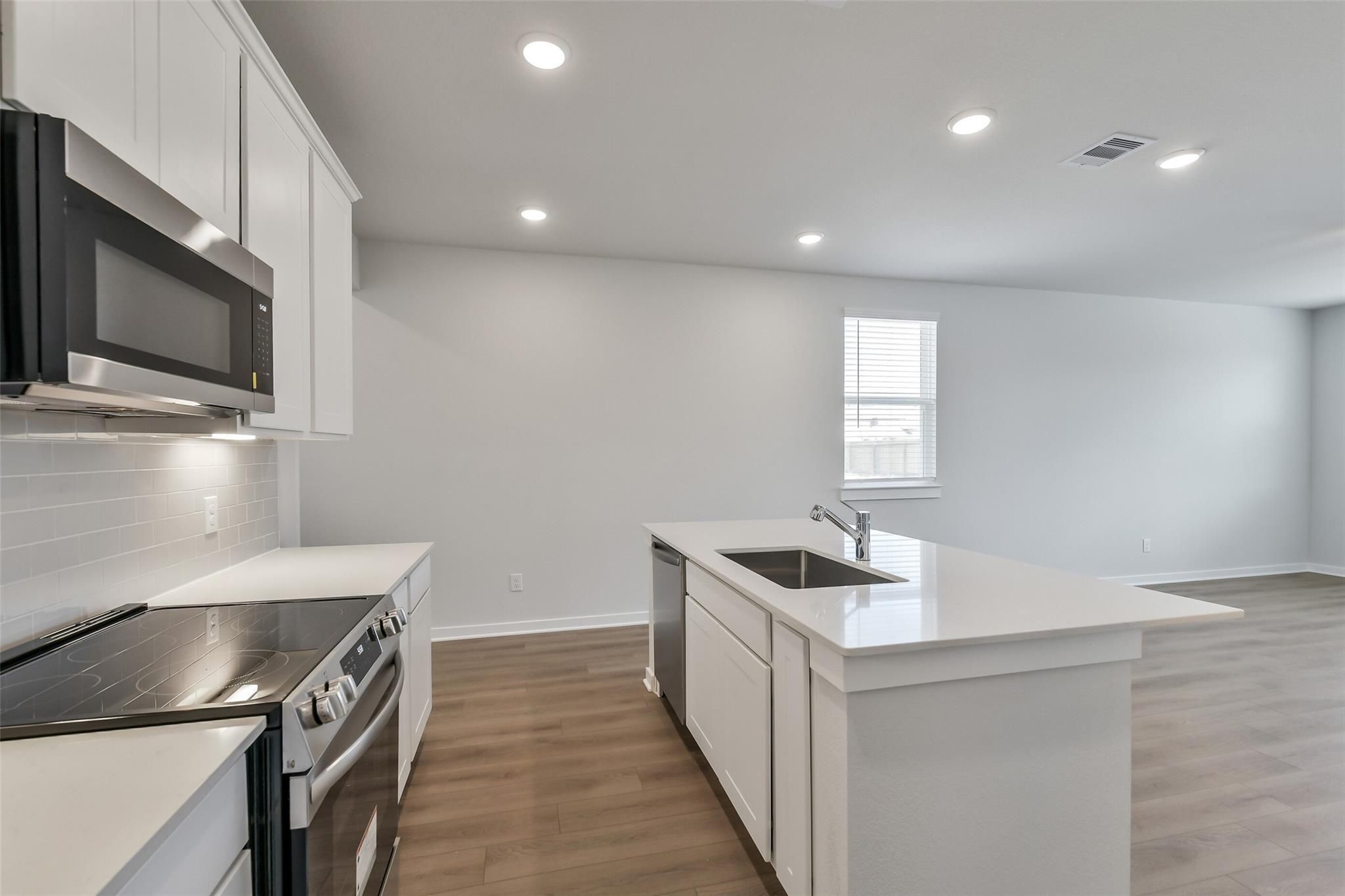 Bright white kitchen with stainless steel appliances, island sink, and hardwood floors in Davidson Homes The Colorado F, Cleveland Texas