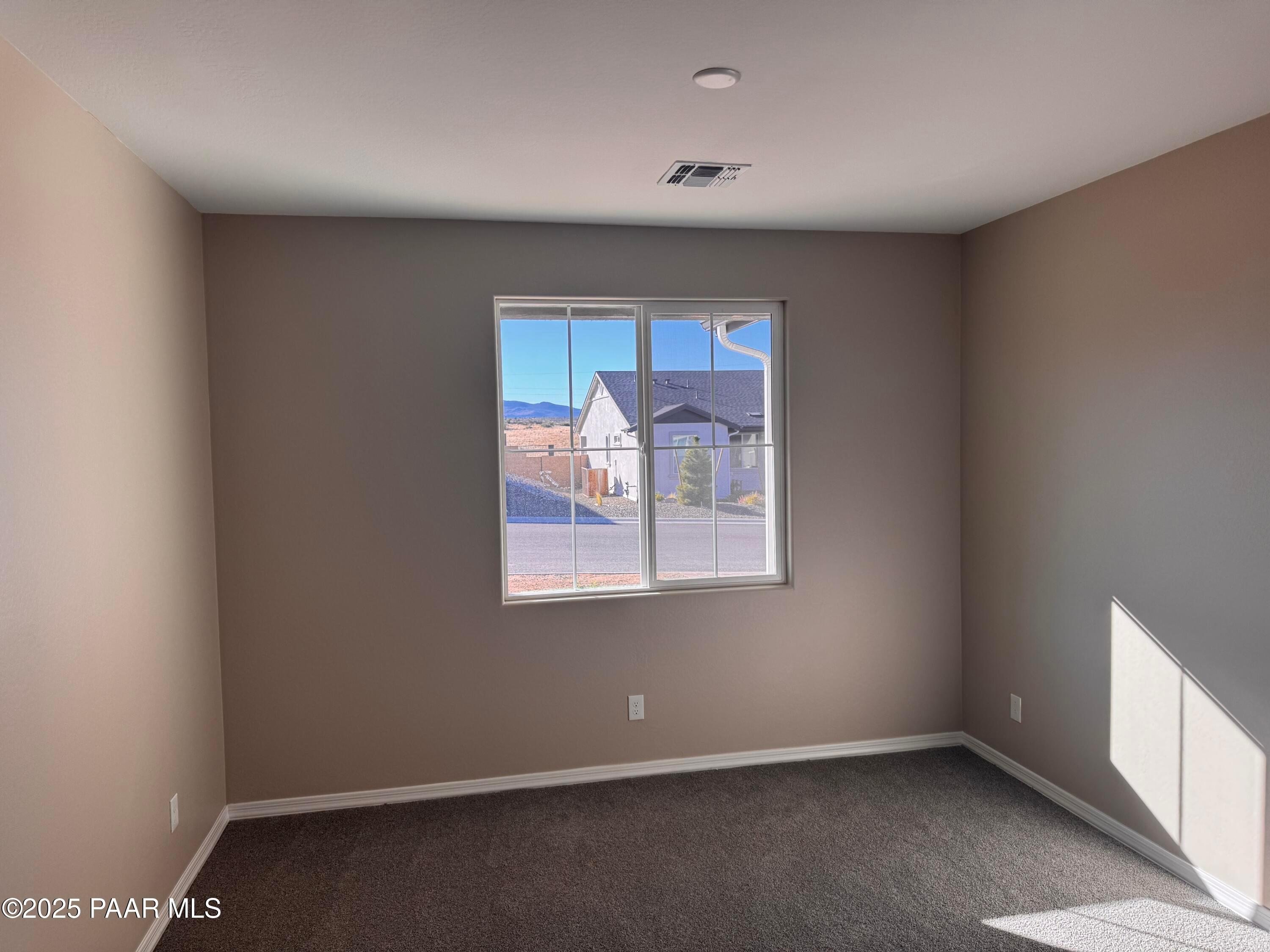 Bright empty bedroom with beige walls, gray carpet, and large window view of Prescott AZ mountains in Davidson Homes Sunrise II A