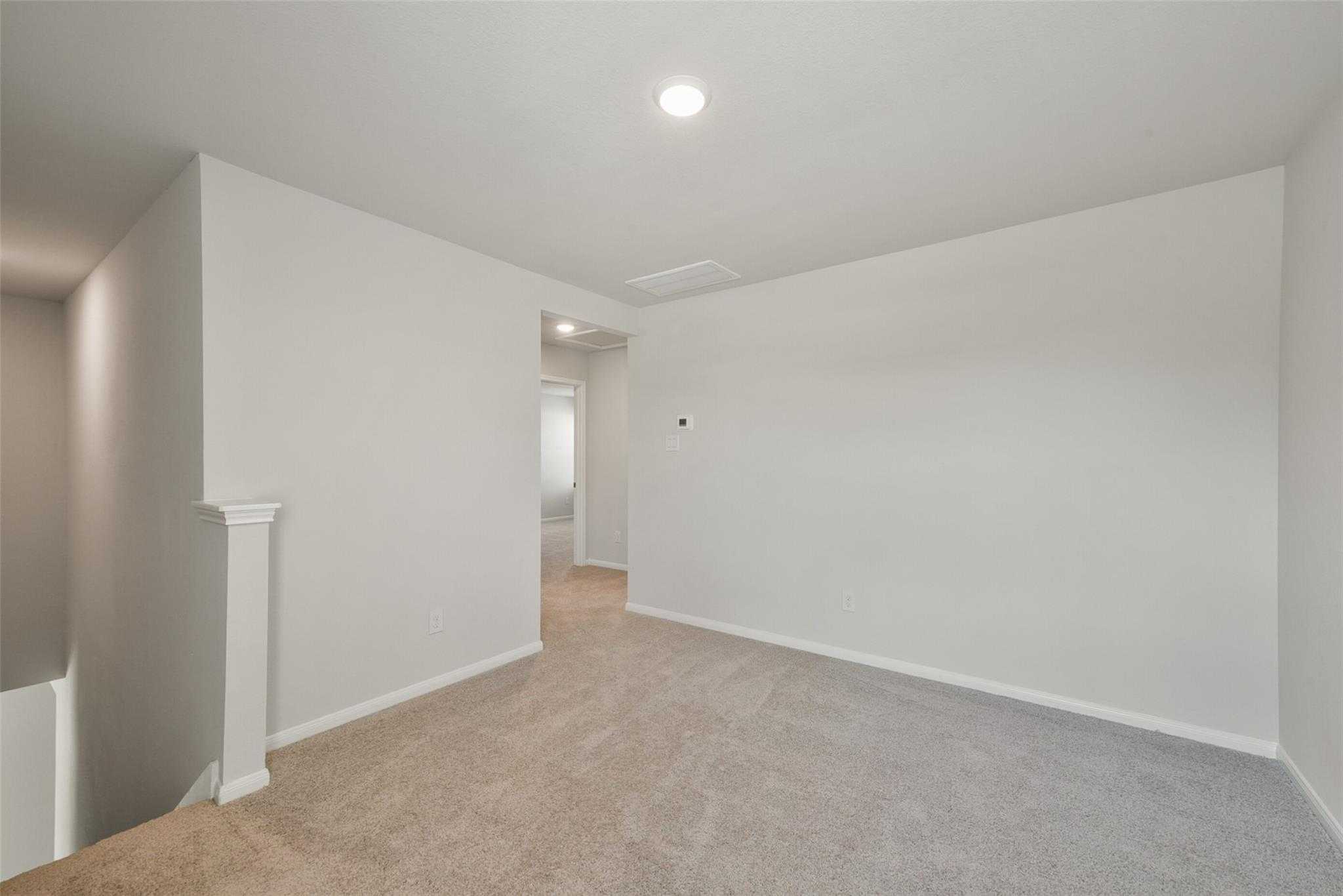 Spacious carpeted upstairs hallway with white walls, recessed lighting, and open doorway in Davidson Homes The Sabine E, Dayton, Texas