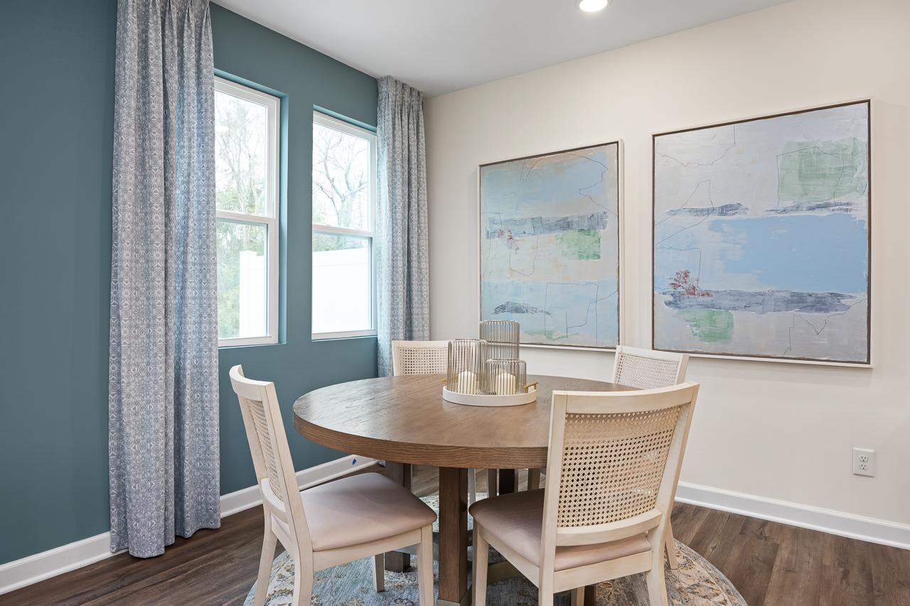Modern dining room in Gregory Village Townhomes Lillington NC with round wooden table, rattan chairs, abstract blue art, and large windows