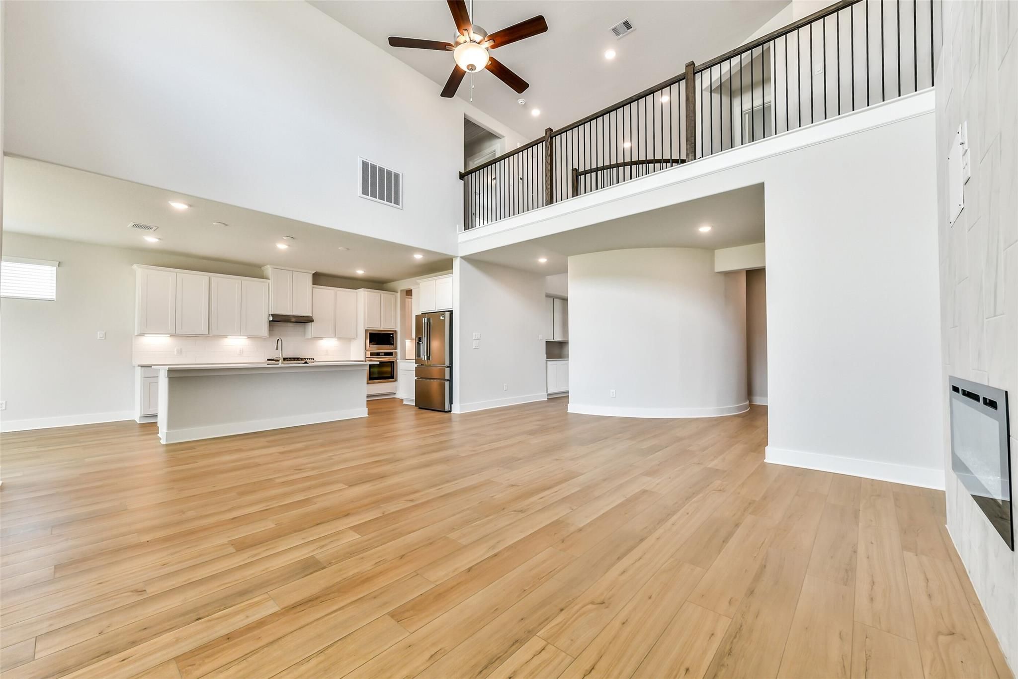 Spacious open kitchen and living area with white cabinets, island, stainless appliances, balcony overlook, hardwood floors in Davidson Homes Victoria A, Texas City