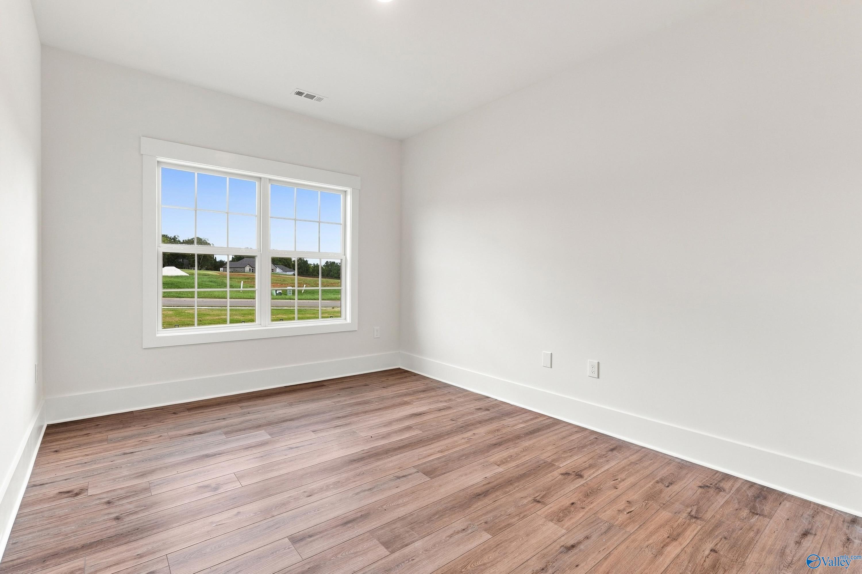 Bright empty bedroom with wood-look flooring and double-pane window in Davidson Homes The Valencia, Riverton Preserve, Huntsville, Alabama