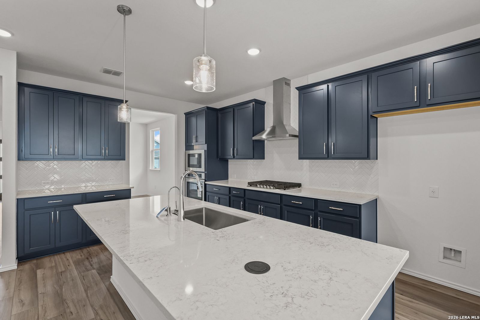 Modern navy blue kitchen cabinets, quartz island sink, stainless steel range hood and appliances in The Glenwood E, Elmendorf, Texas