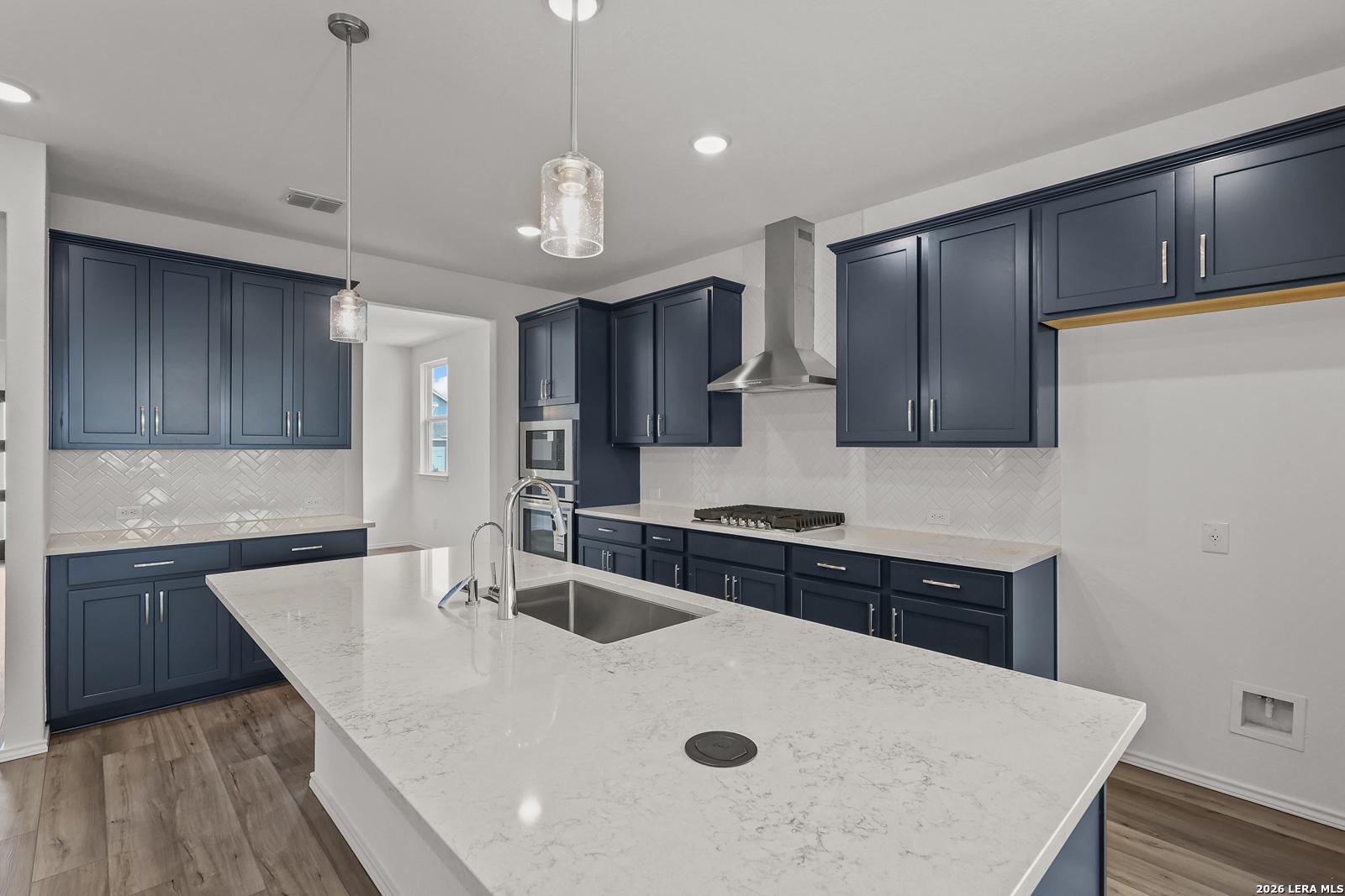 Modern navy blue kitchen cabinets, quartz island sink, stainless steel range hood and appliances in The Glenwood E, Elmendorf, Texas