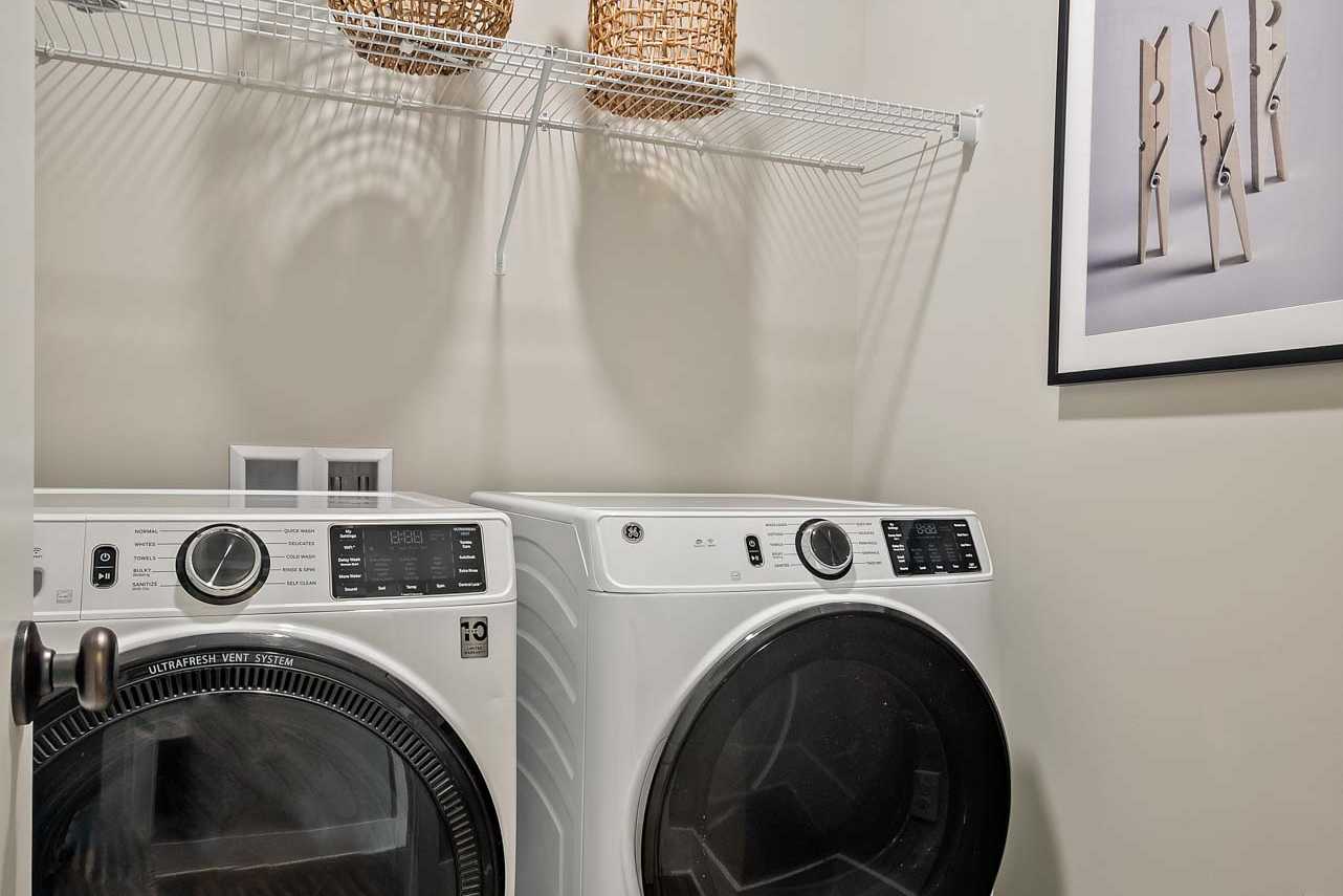Modern laundry room at Heritage Lakes in New Market Alabama with white front-load washer dryer, wicker baskets on wire shelving, and hardwood floors