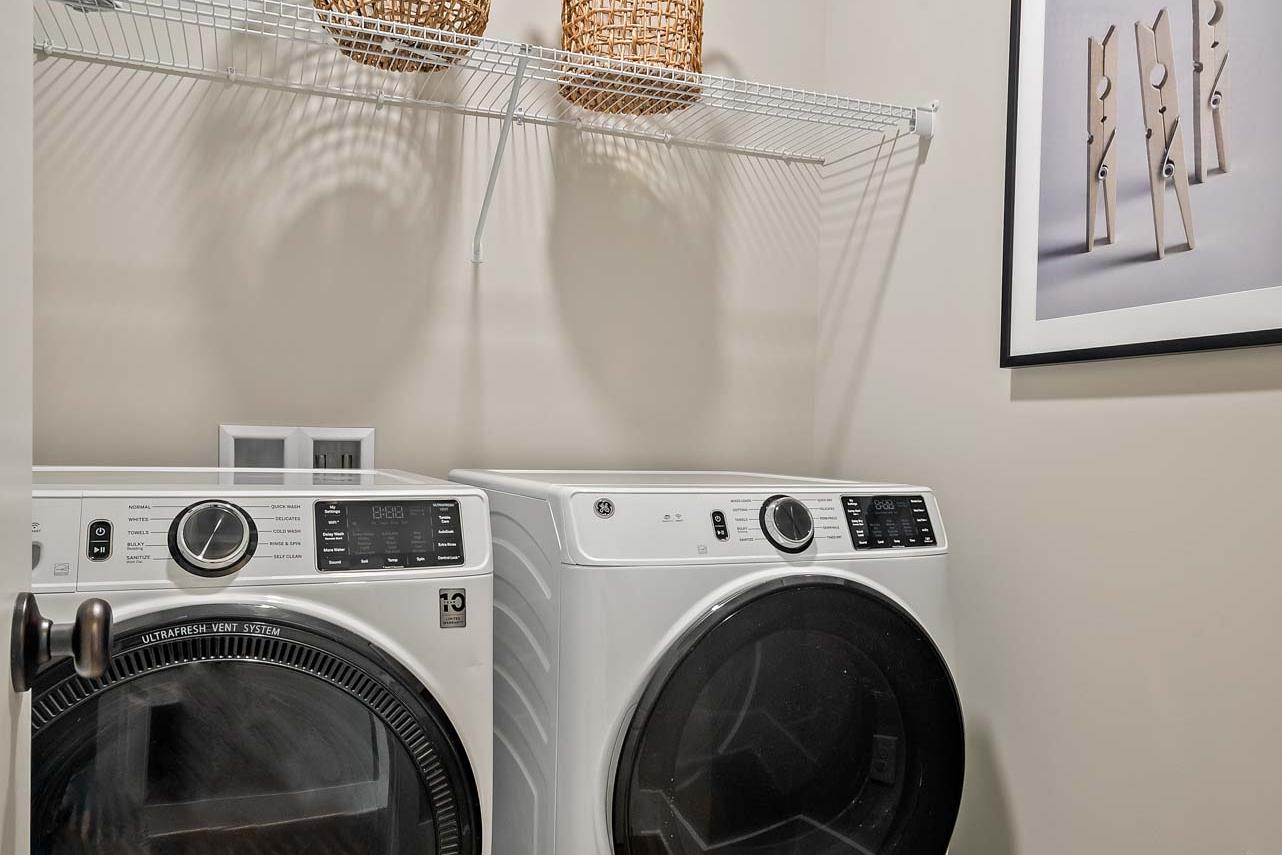 Modern laundry room at Heritage Lakes in New Market Alabama with white front-load washer dryer, wicker baskets on wire shelving, and hardwood floors