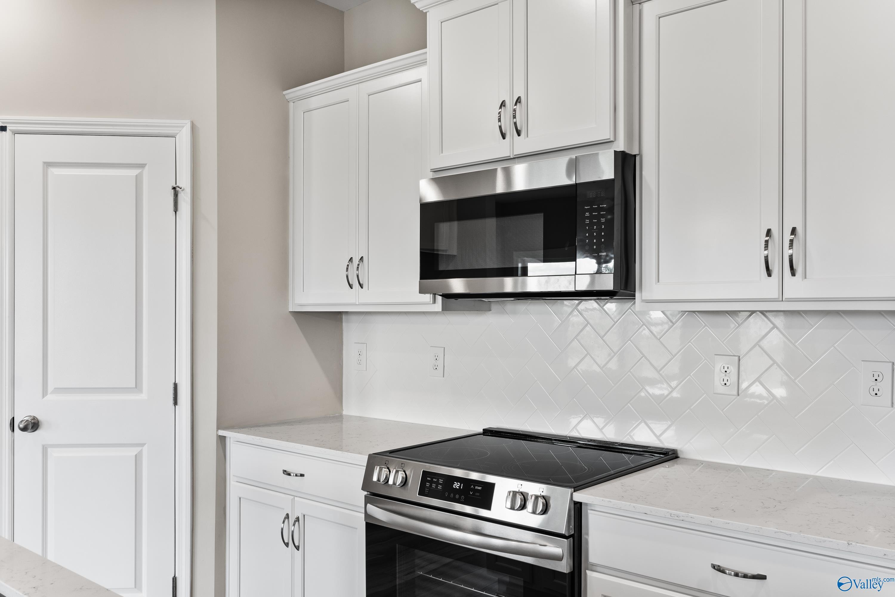 Modern white kitchen with stainless steel microwave, oven, and subway tile backsplash in Davidson Homes The Daphne C, Harvest, AL