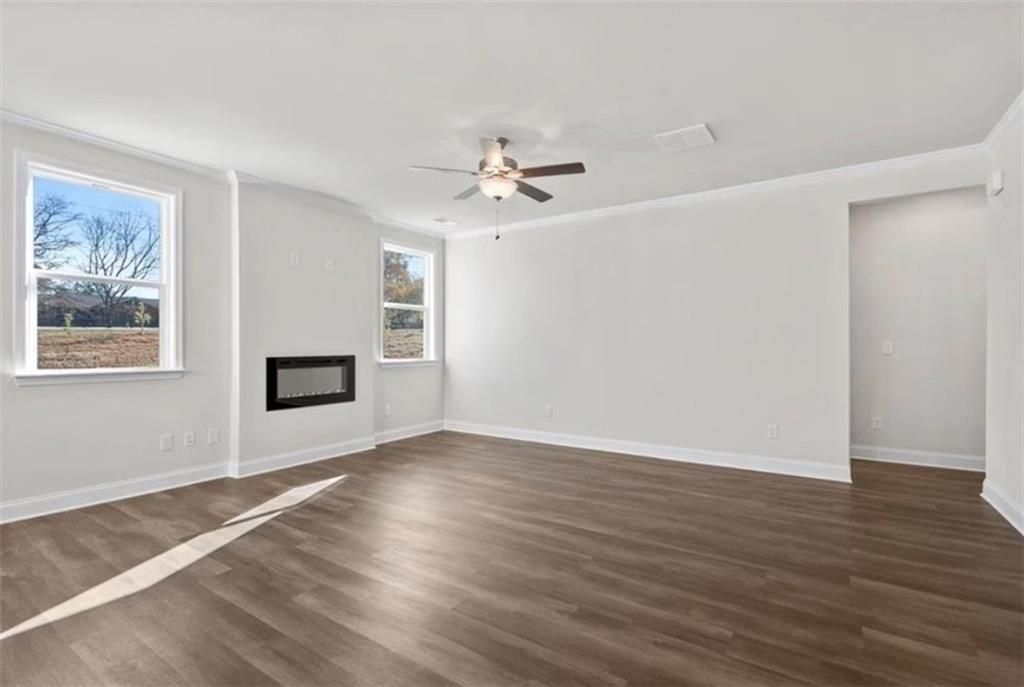 Spacious living room with fireplace and wood-style flooring in The Ash C floor plan at Wehunt Meadows, Hoschton, Georgia.