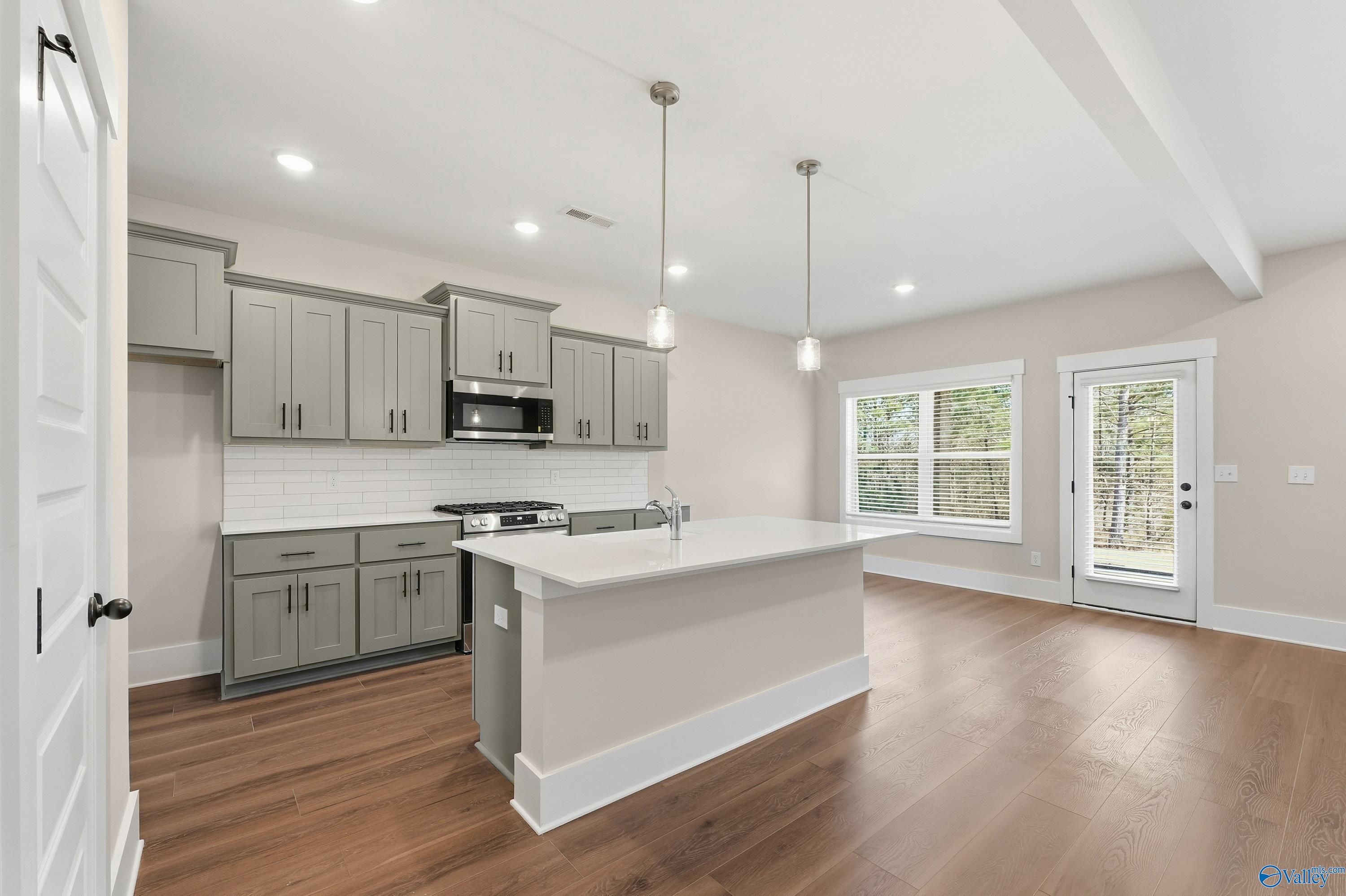 Modern open-concept kitchen with gray shaker cabinets, white subway backsplash, quartz island, and stainless appliances in Davidson Homes The Shelby A, Athens, AL