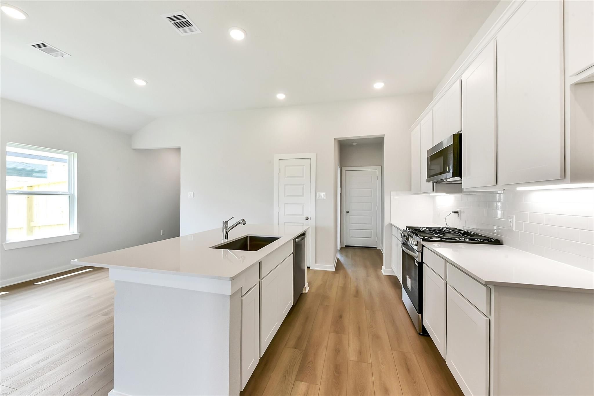 Modern white kitchen with quartz island, stainless gas range, and open layout in Davidson Homes The Costa B, Dayton, Texas