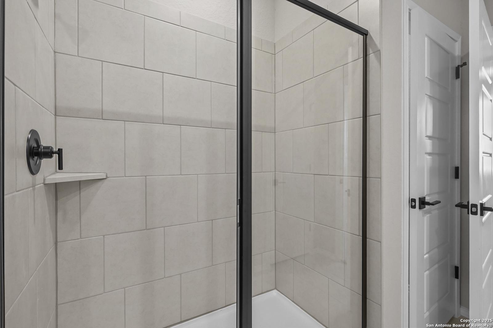 Modern master bathroom with glass shower enclosure, neutral tile walls, and sleek fixtures in Davidson Homes The Brazos C, San Antonio