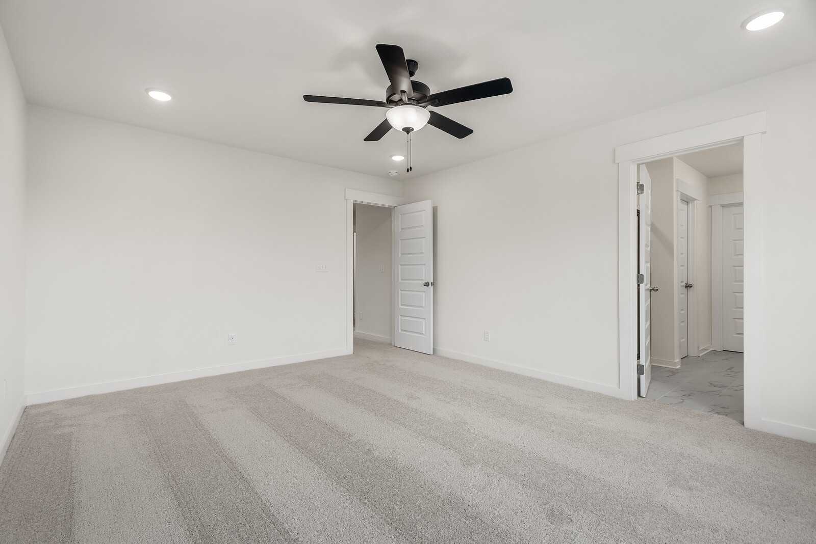 Spacious secondary bedroom with plush gray carpet, ceiling fan, and en-suite bath door in Davidson Homes The Logan C, Gallatin, TN