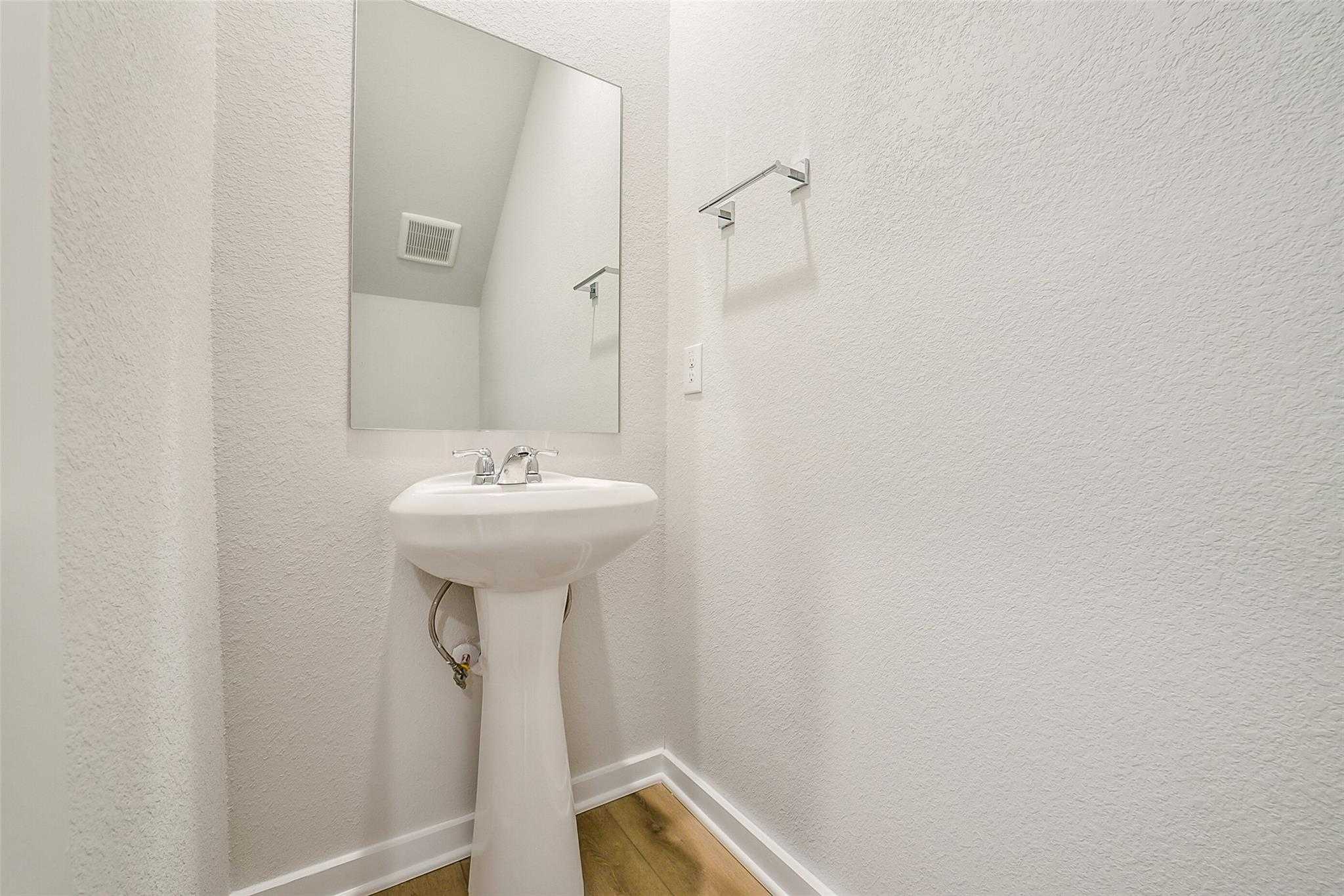 Elegant powder room with white pedestal sink, frameless mirror, and towel bar in Davidson Homes The Blanco E, Magnolia, Texas