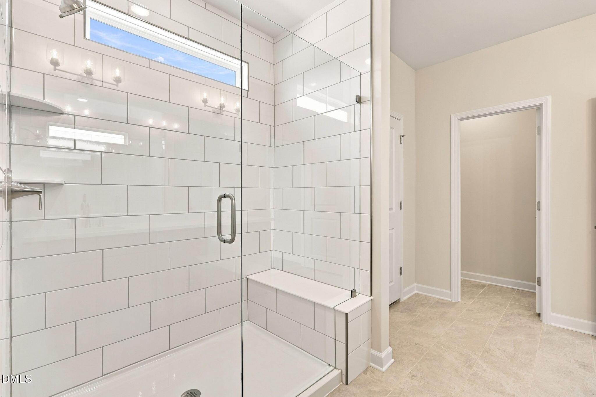 Walk-in tiled shower with glass door and built-in bench in The Magnolia B floor plan at Retreat at North Main, Lillington.