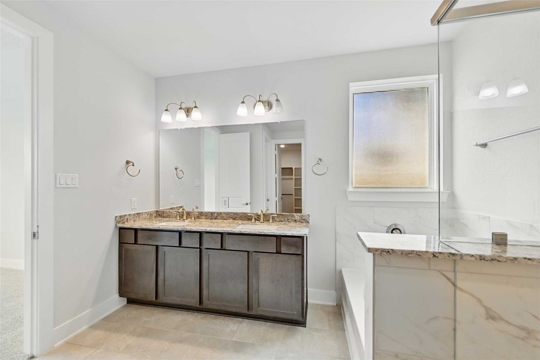 Elegant master bathroom with double granite vanity, soaking tub, and frosted window in Davidson Homes The Philip A, Lago Mar, Texas