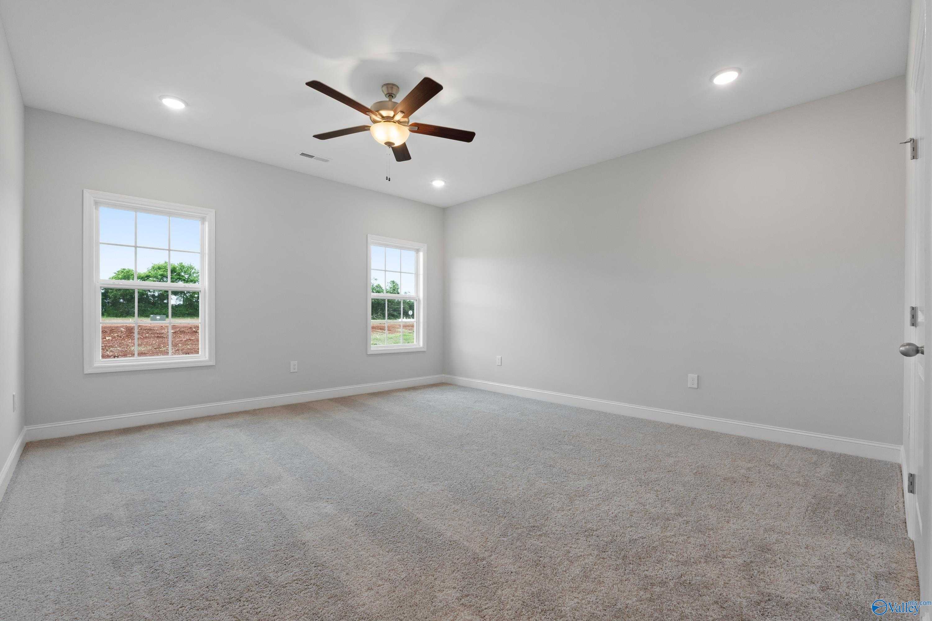Spacious empty bedroom with gray walls, carpet floor, ceiling fan, and large windows in Davidson Homes The Rockford B, Toney, Alabama