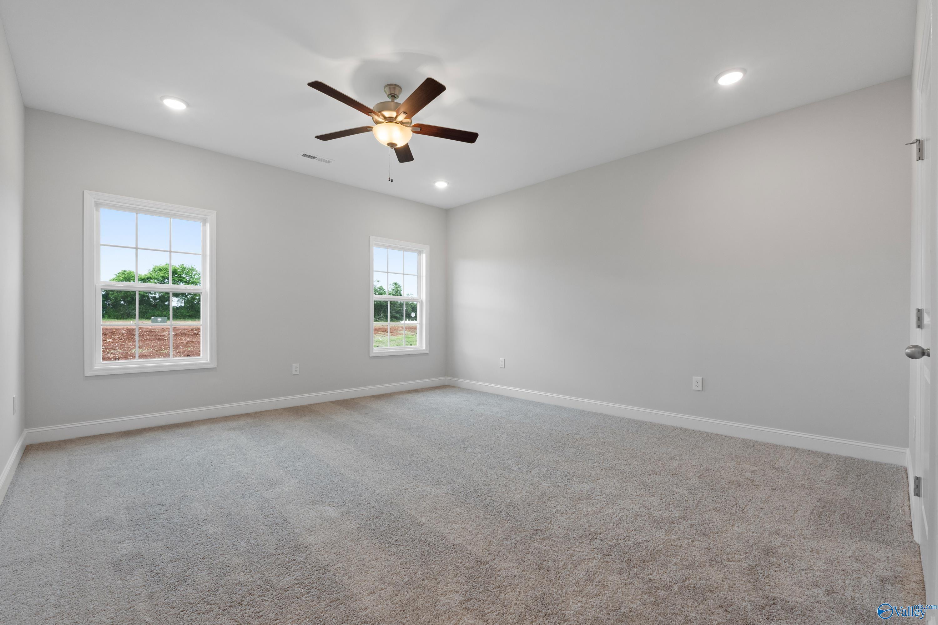 Spacious empty bedroom with gray walls, plush carpet, ceiling fan, and large windows in Davidson Homes The Rockford B, Toney, AL