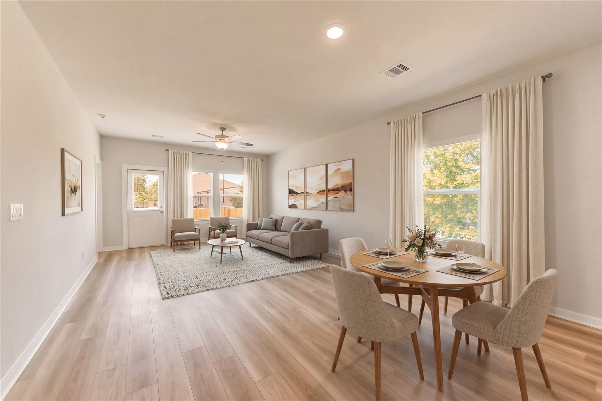 Open living dining room with hardwood floors, gray sofa, round wood table, and large windows in Davidson Homes The Frio G, Magnolia Texas