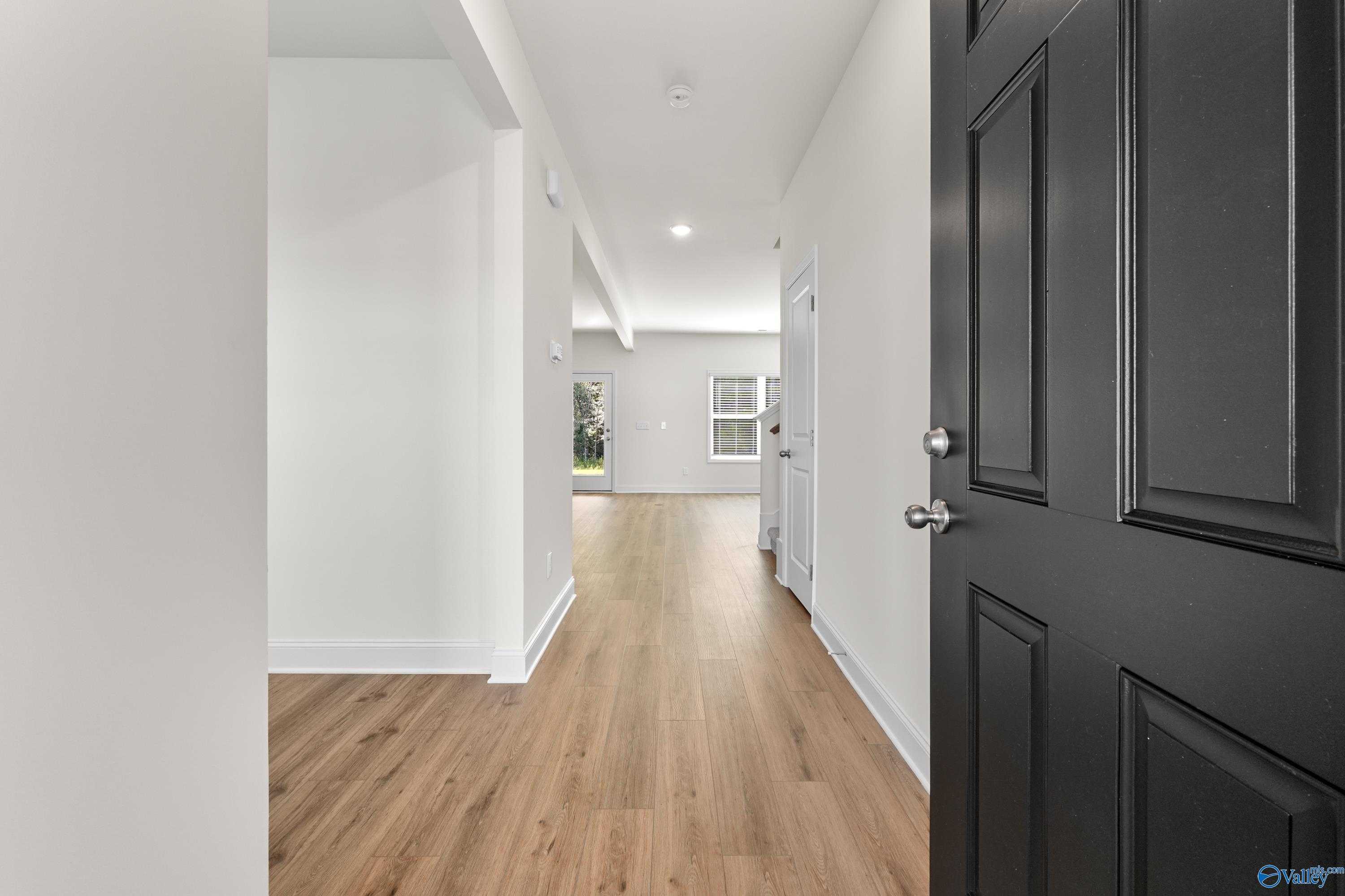 Bright hallway with hardwood floors, white walls, and open doorways in Davidson Homes The Shelby A, Athens, Alabama