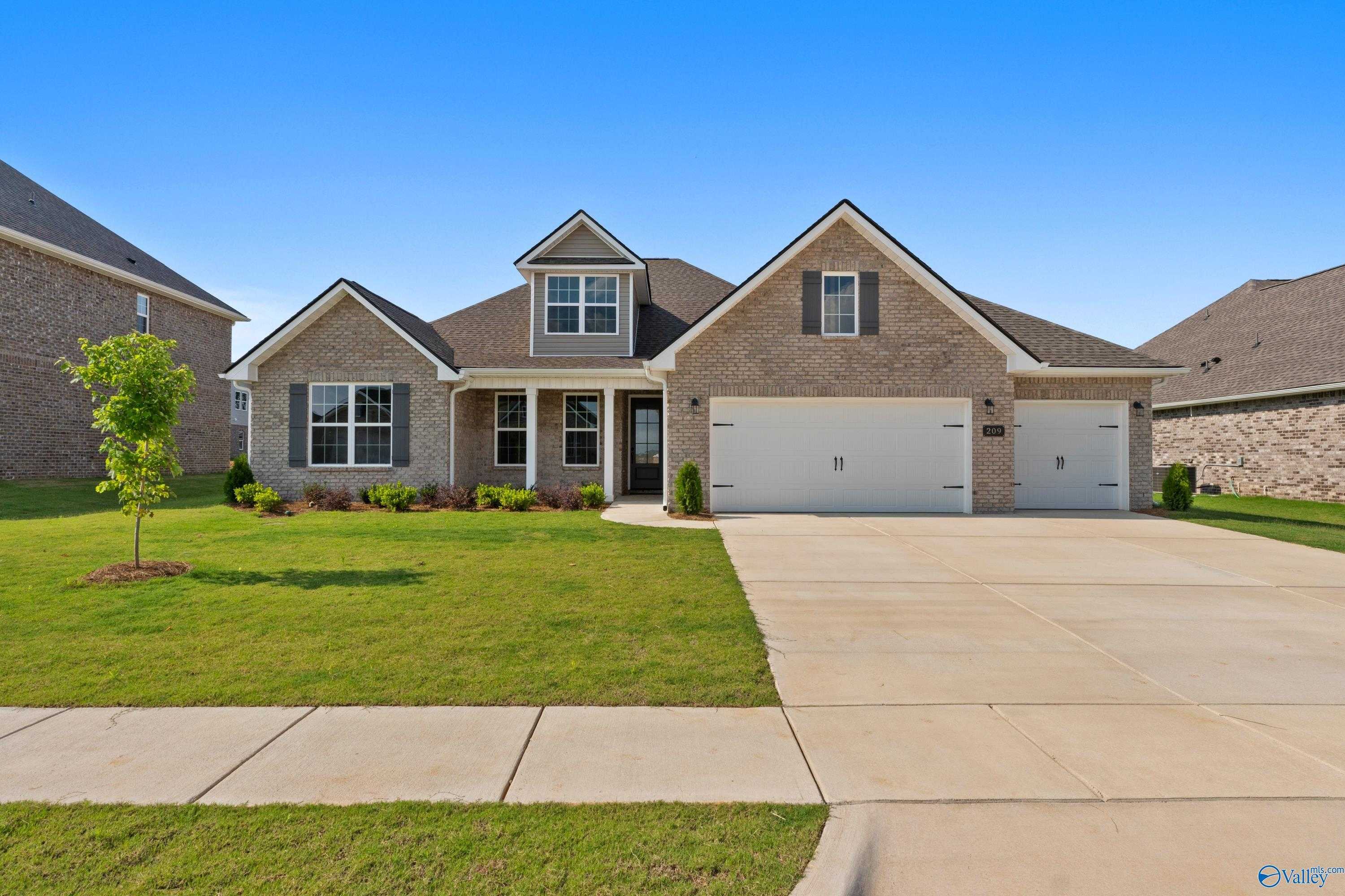 Tan brick ranch-style home with 3-car garage, gabled roof, front porch, and manicured lawn in Kendall Farms, Toney, Alabama