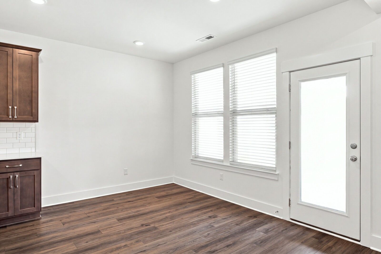 Bright dining area with hardwood-look flooring, white glass-panel door, and dark wood cabinetry in Davidson Homes The Willow C, Gallatin TN
