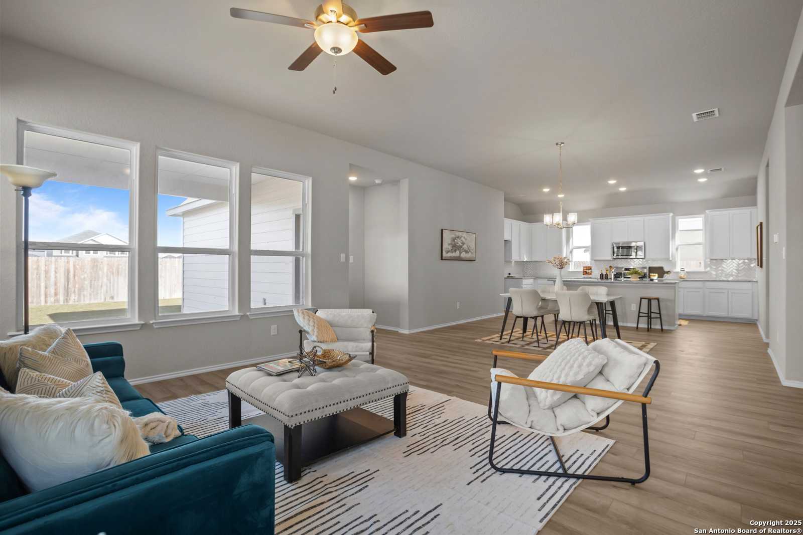 Open-concept living room with blue velvet sofa, ceiling fan, and bar stools at kitchen island in Davidson Homes The Collin B, Seguin, Texas