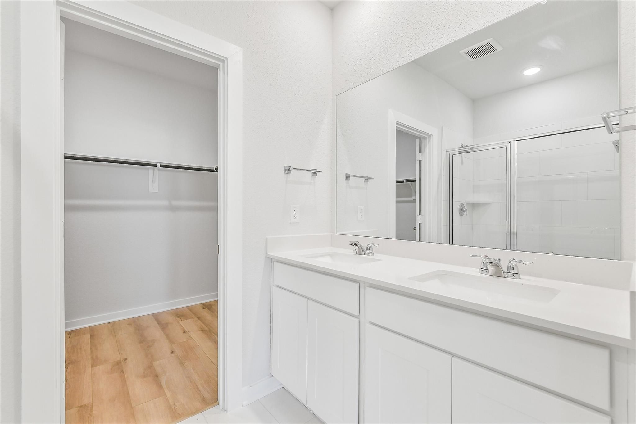 Modern master bathroom featuring double vanity, frameless shower, and adjacent walk-in closet in Davidson Homes Blanco E, Magnolia TX