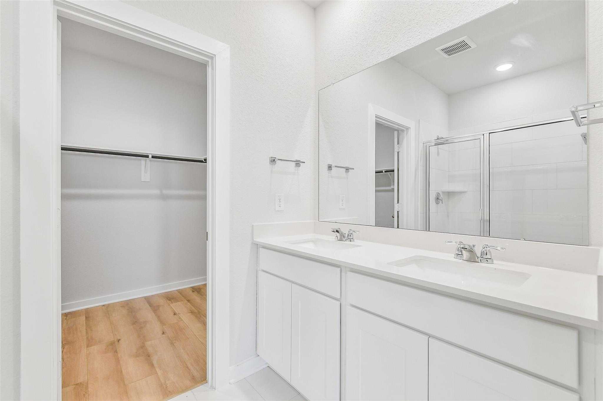 Modern master bathroom featuring double vanity, frameless shower, and adjacent walk-in closet in Davidson Homes Blanco E, Magnolia TX