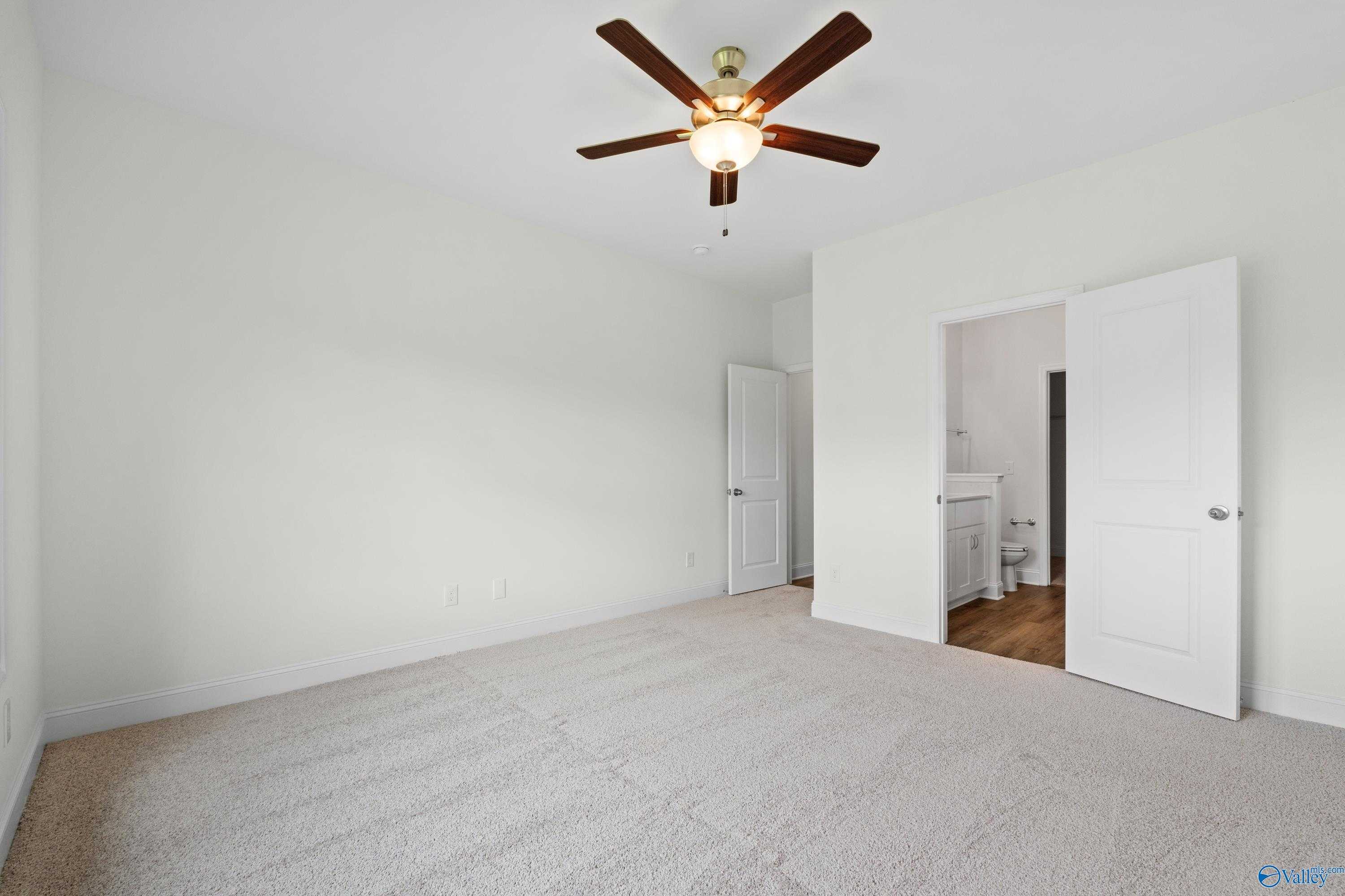 Spacious bedroom with ceiling fan, white walls, carpet floor, and en-suite bath in Davidson Homes The Asheville C, Athens, Alabama