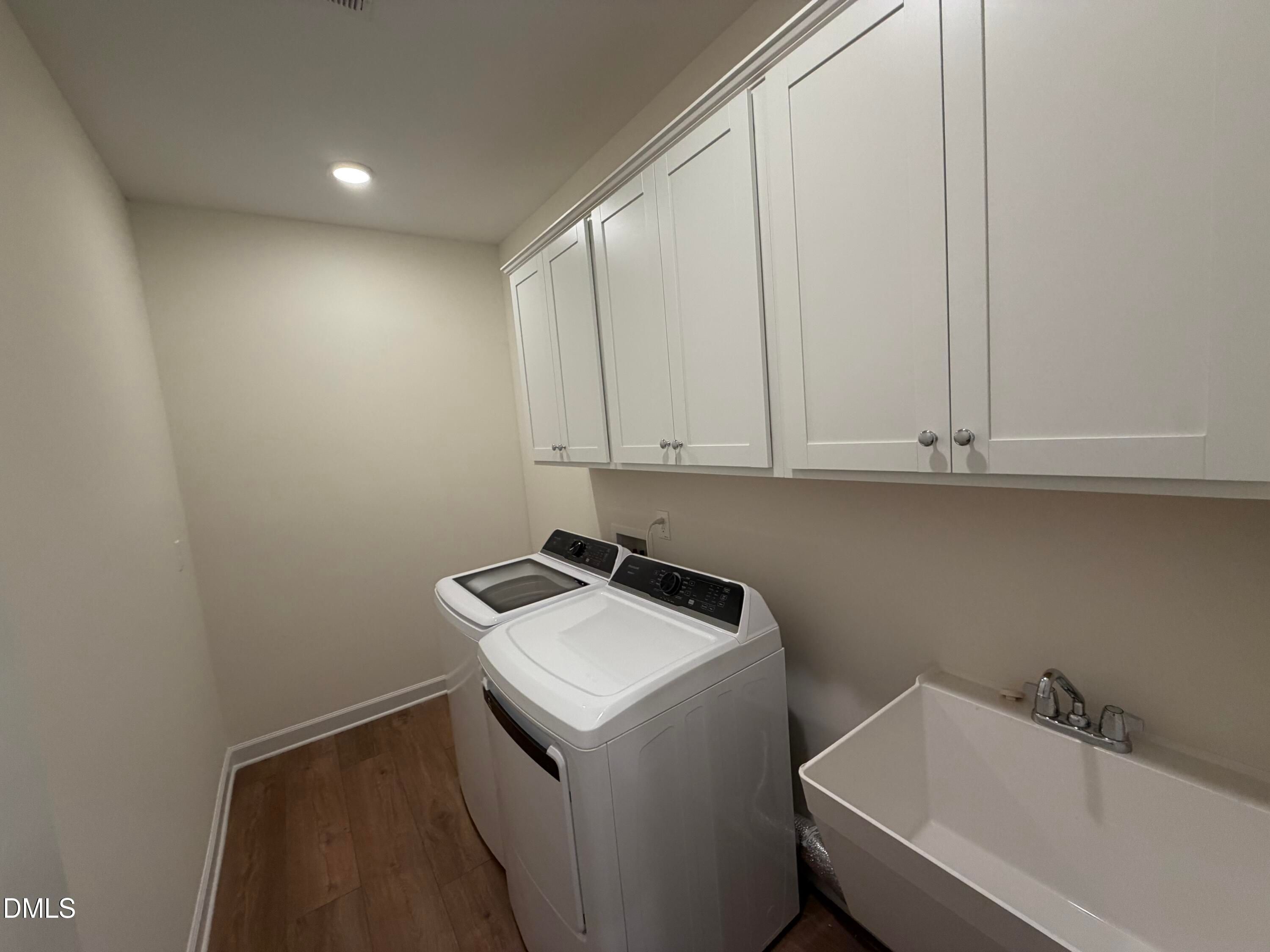 Laundry room with white cabinetry, washer and dryer, utility sink, and wood-look flooring in Davidson Homes The Ashport M, Wendell Ridge.
