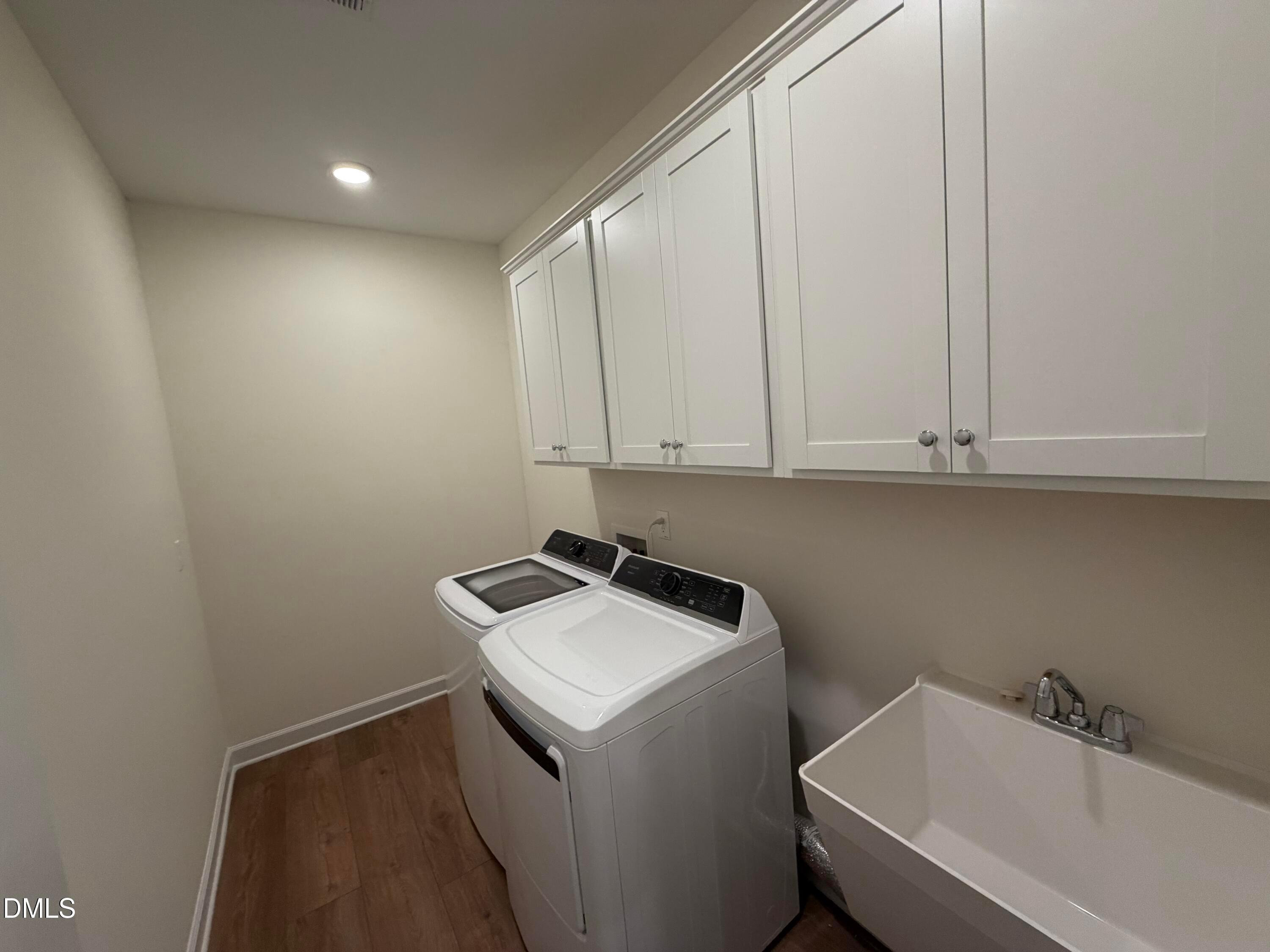 Laundry room with white cabinetry, washer and dryer, utility sink, and wood-look flooring in Davidson Homes The Ashport M, Wendell Ridge.
