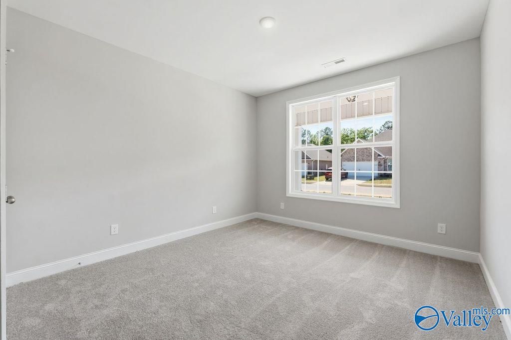 Empty bedroom with light gray walls, plush carpet, and large window overlooking neighborhood in The Harrison home, Hartselle, Alabama
