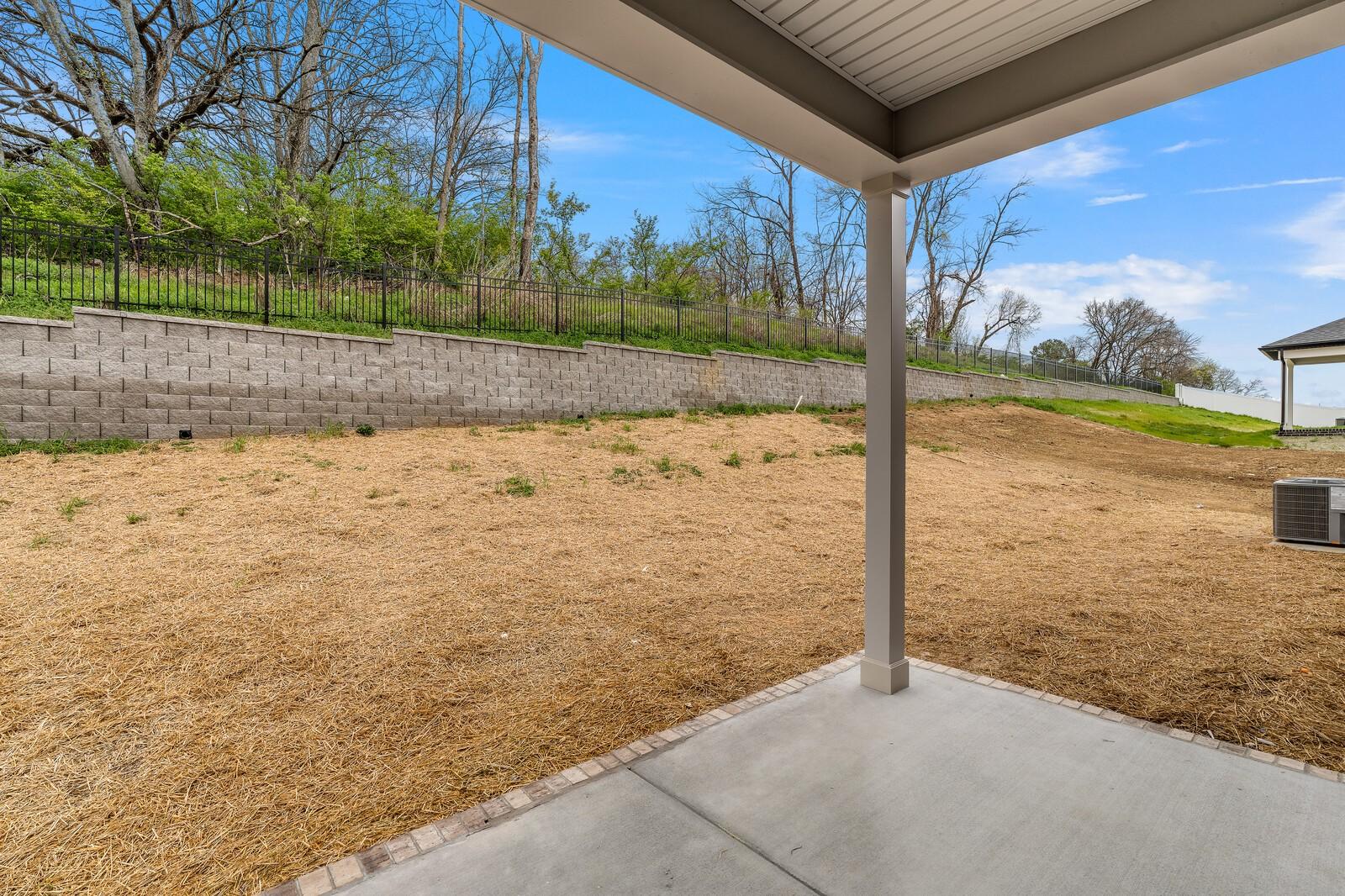 Covered back patio with concrete slab overlooking sloped dirt yard, retaining wall, and wooded hillside in Gallatin, TN home
