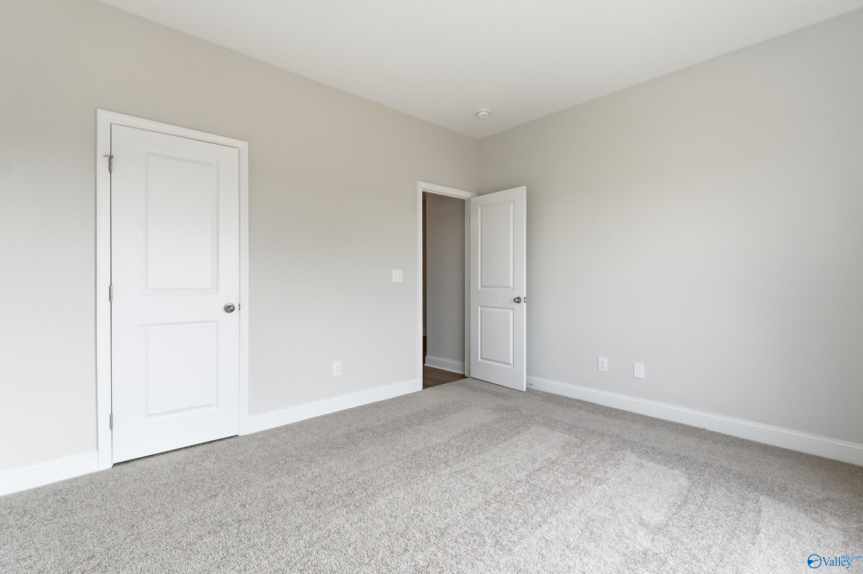 Spacious empty bedroom with beige walls, white doors, and carpet flooring in Davidson Homes The Daphne C, Toney, Alabama