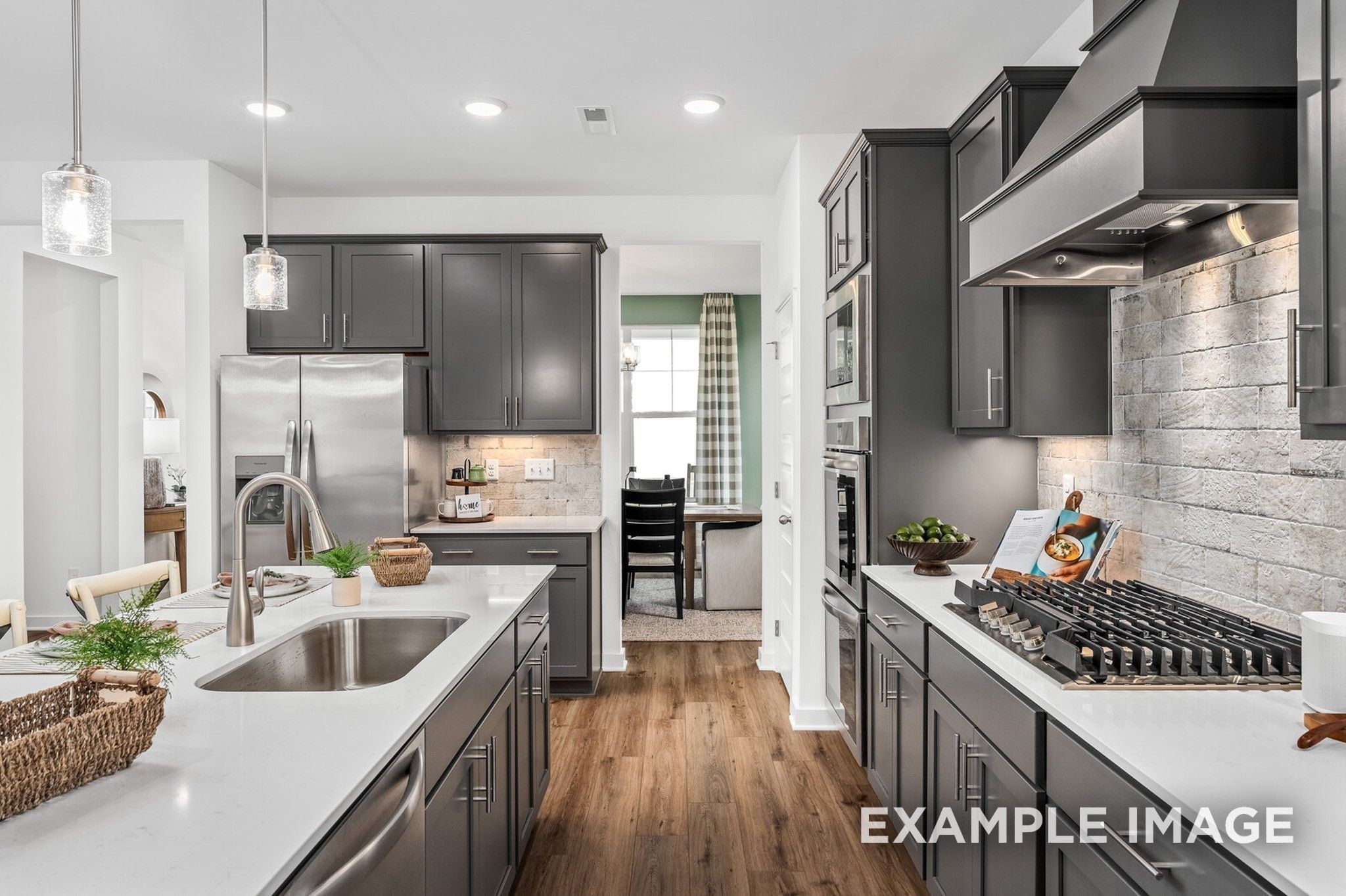 Modern kitchen with gray cabinets, quartz countertops, and brick backsplash in The Ash A floor plan at Woods Crossing.