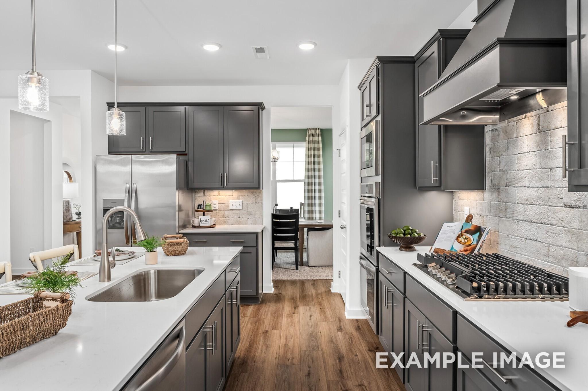 Modern kitchen with gray cabinets, quartz countertops, and brick backsplash in The Ash A floor plan at Woods Crossing.