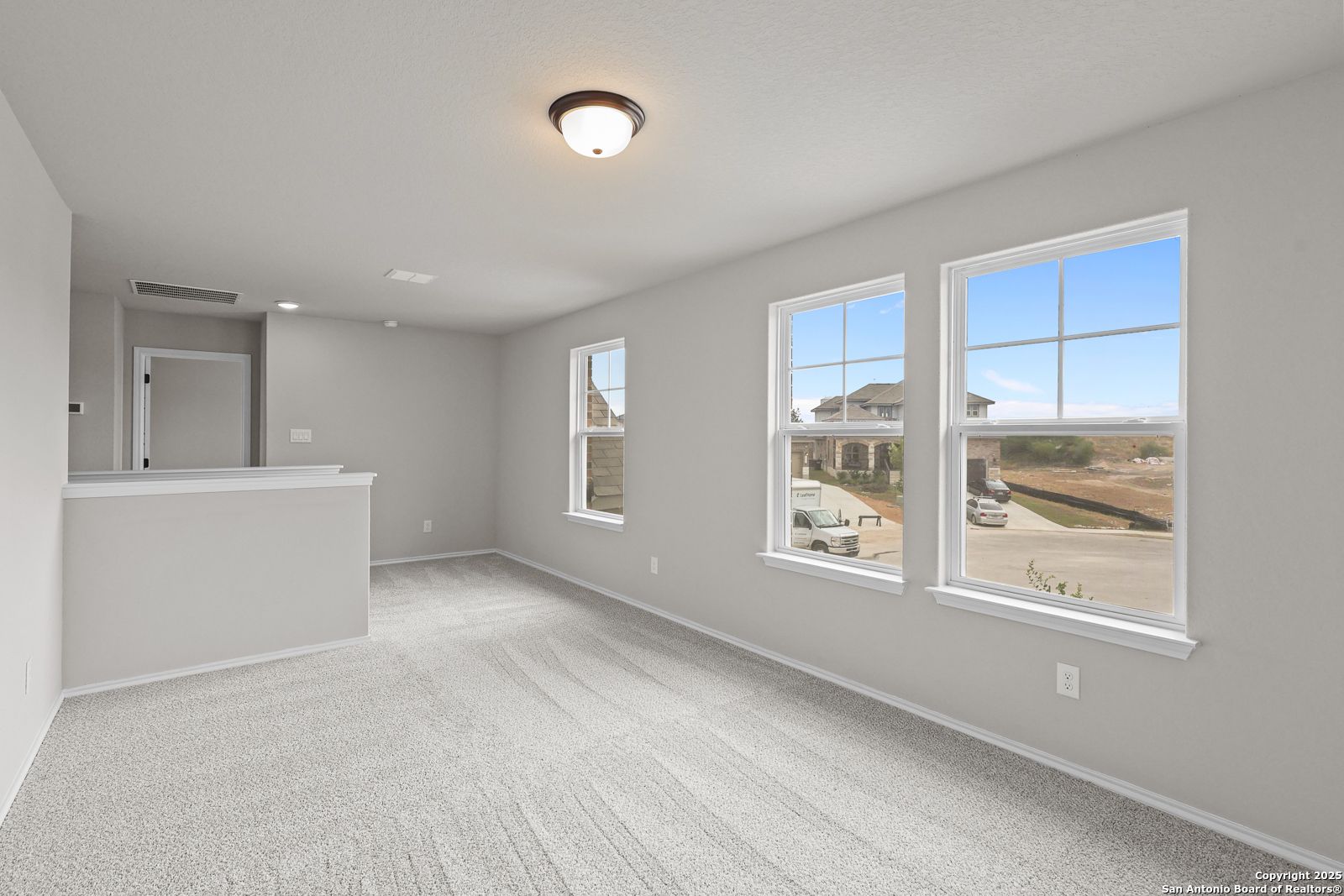 Bright upstairs loft with built-in bar, gray carpeted floors, and large windows overlooking Royal Crest neighborhood in The Murray J home, San Antonio