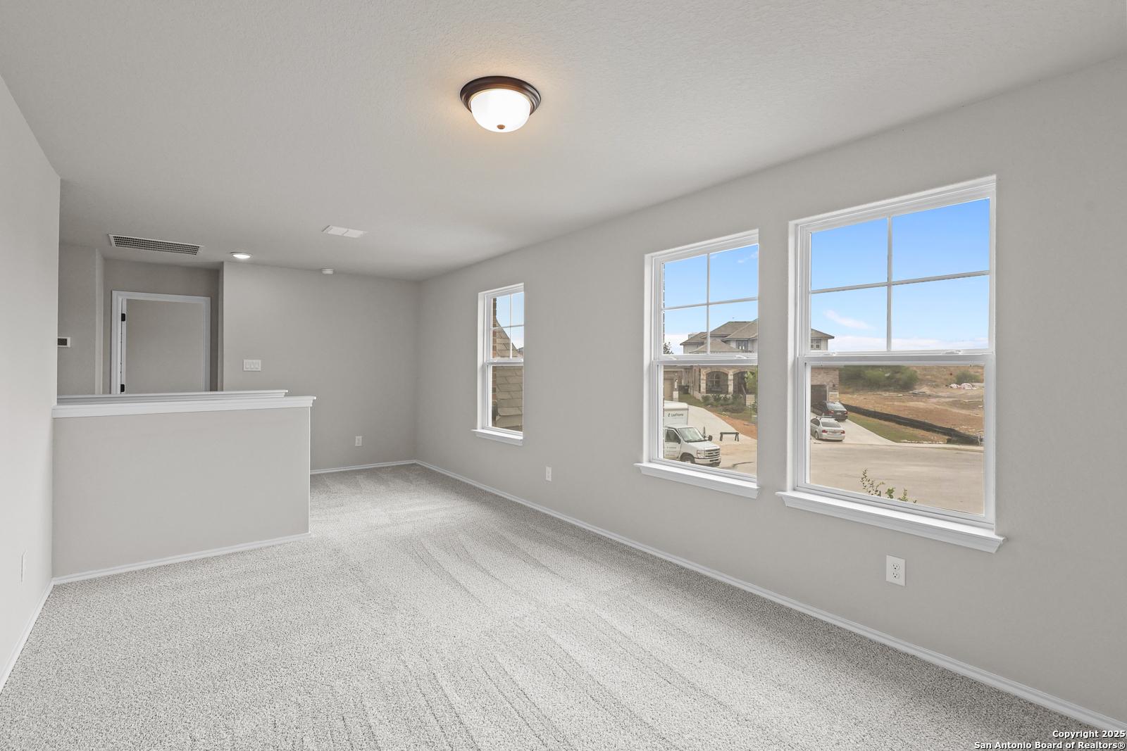 Bright upstairs loft with built-in bar, gray carpeted floors, and large windows overlooking Royal Crest neighborhood in The Murray J home, San Antonio