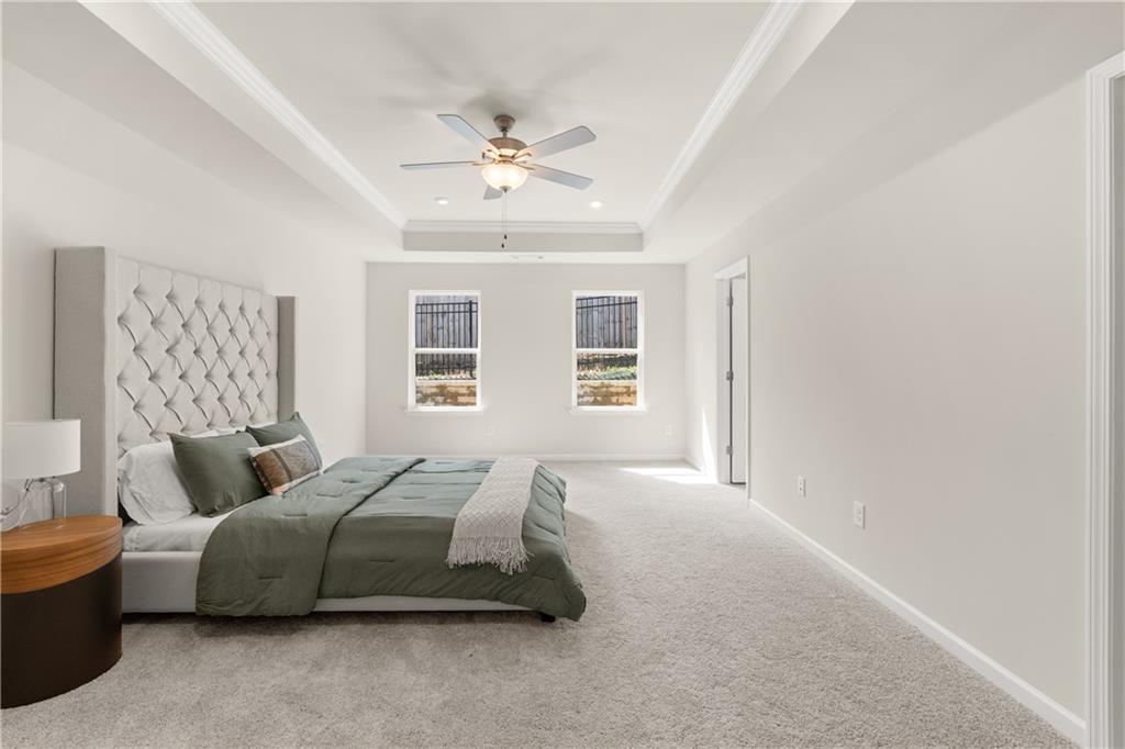 Elegant master bedroom with tufted white headboard, green bedding, tray ceiling fan, and dual windows in Davidson Homes The Marion B, Kennesaw, GA