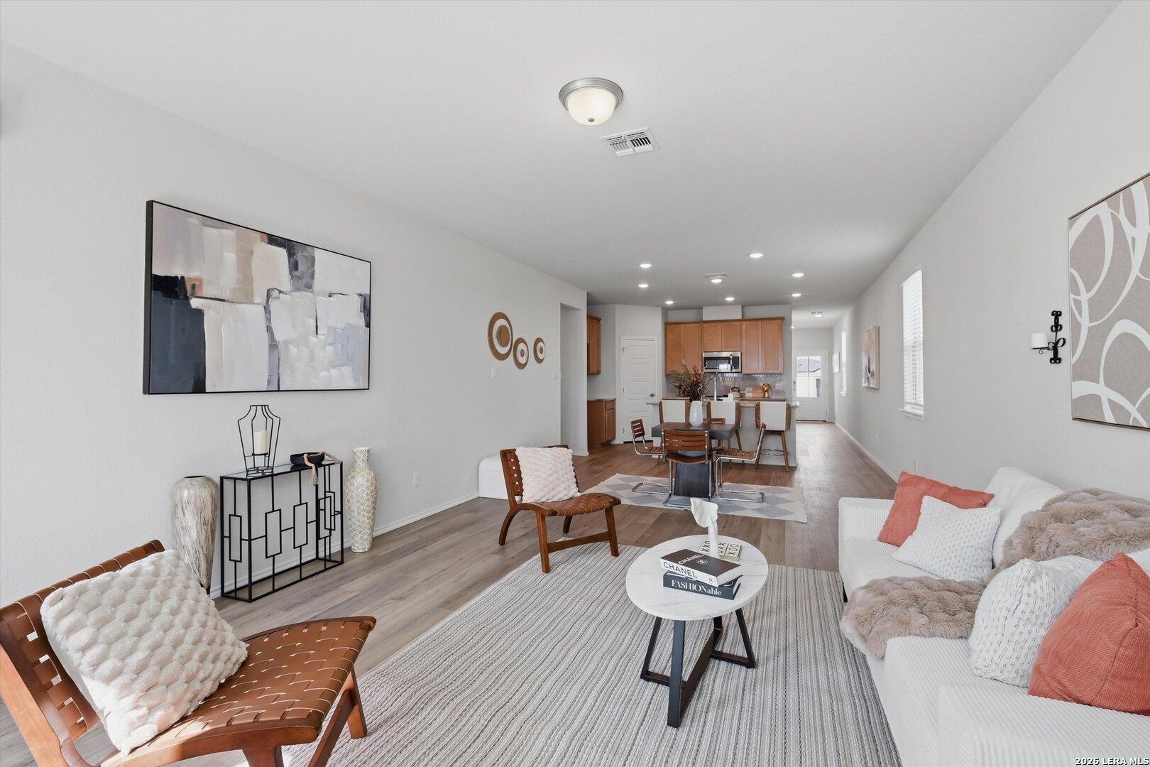 Modern open-concept living room with white sofa, rattan chairs, wooden floors, and dining area in Davidson Homes The Sabine A, San Antonio