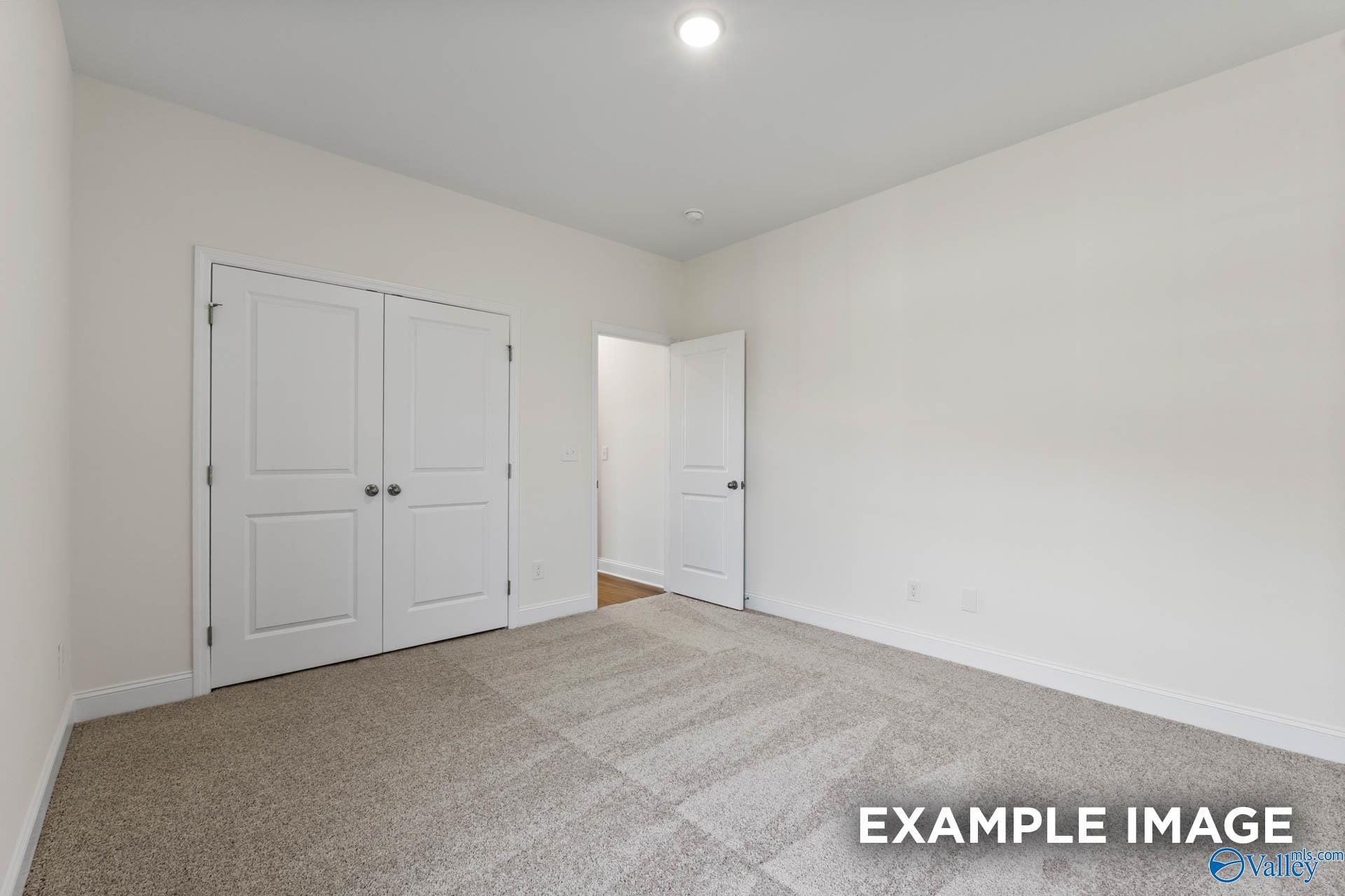 Spacious bedroom with white double closet doors and adjacent bath entry in Davidson Homes The Harrison C, Athens, Alabama