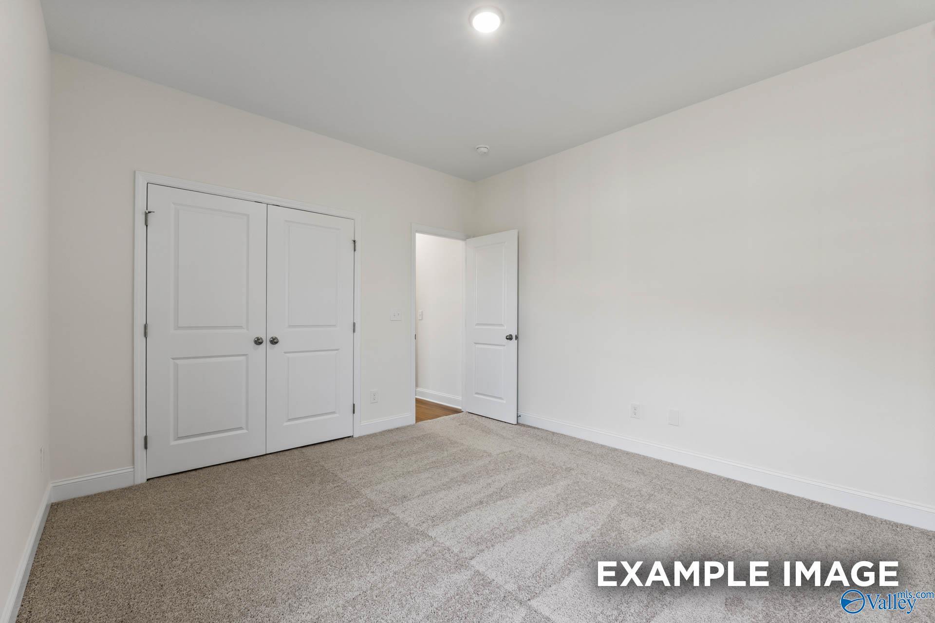 Spacious bedroom with white double closet doors and adjacent bath entry in Davidson Homes The Harrison C, Athens, Alabama