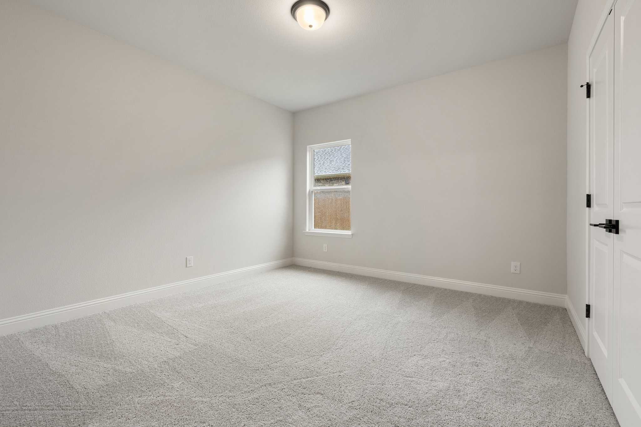 Spacious empty bedroom in The Harrison C home with beige walls, gray carpet, large window, and double closet doors