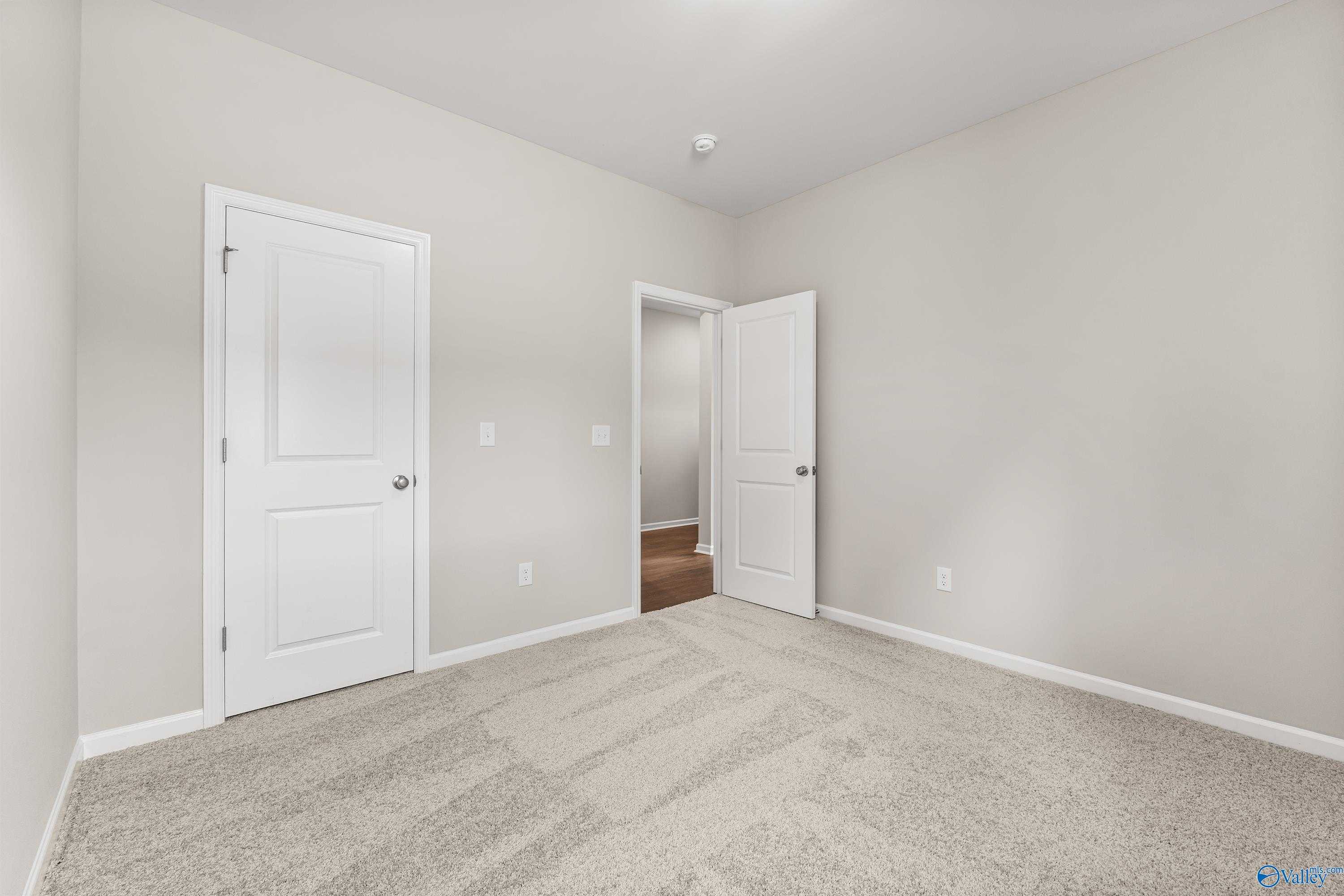 Spacious secondary bedroom with neutral walls, beige carpet, and open doors in Davidson Homes The Phoenix, Fayetteville, TN