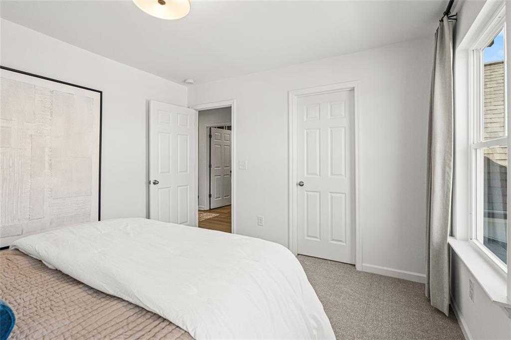 Cozy secondary bedroom with queen bed, white bedding, closet doors, and large window in Davidson Homes The Hickory B, Hoschton, GA