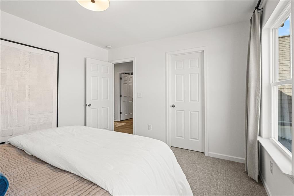 Cozy secondary bedroom with queen bed, white bedding, closet doors, and large window in Davidson Homes The Hickory B, Hoschton, GA