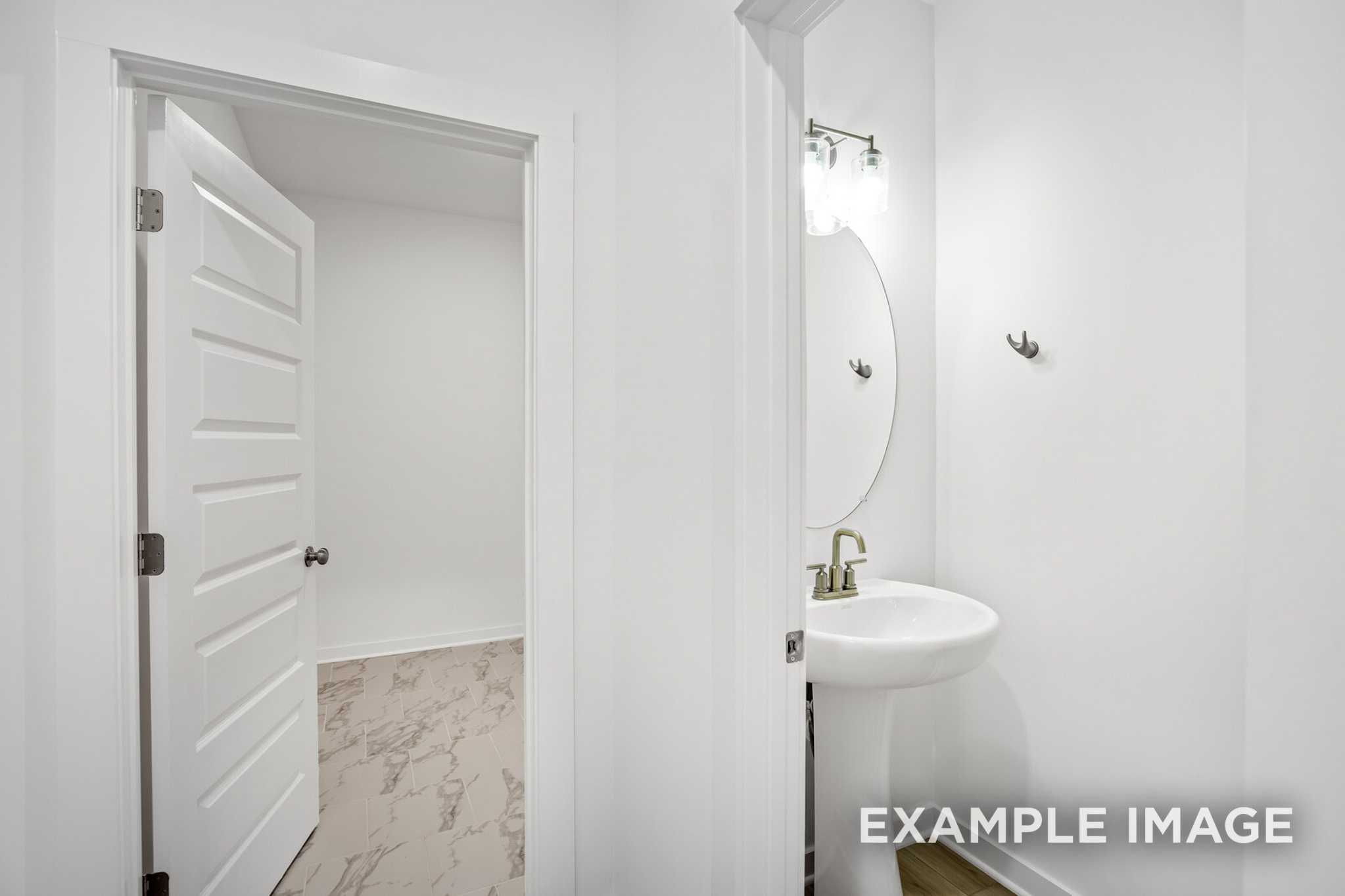 Modern powder room in The Murray B featuring round mirror, gold faucet pedestal sink, and adjacent walk-in closet